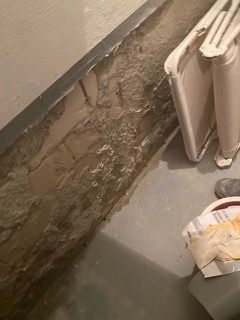 Neben einer Backsteinmauer steht auf dem Boden ein Mülleimer.