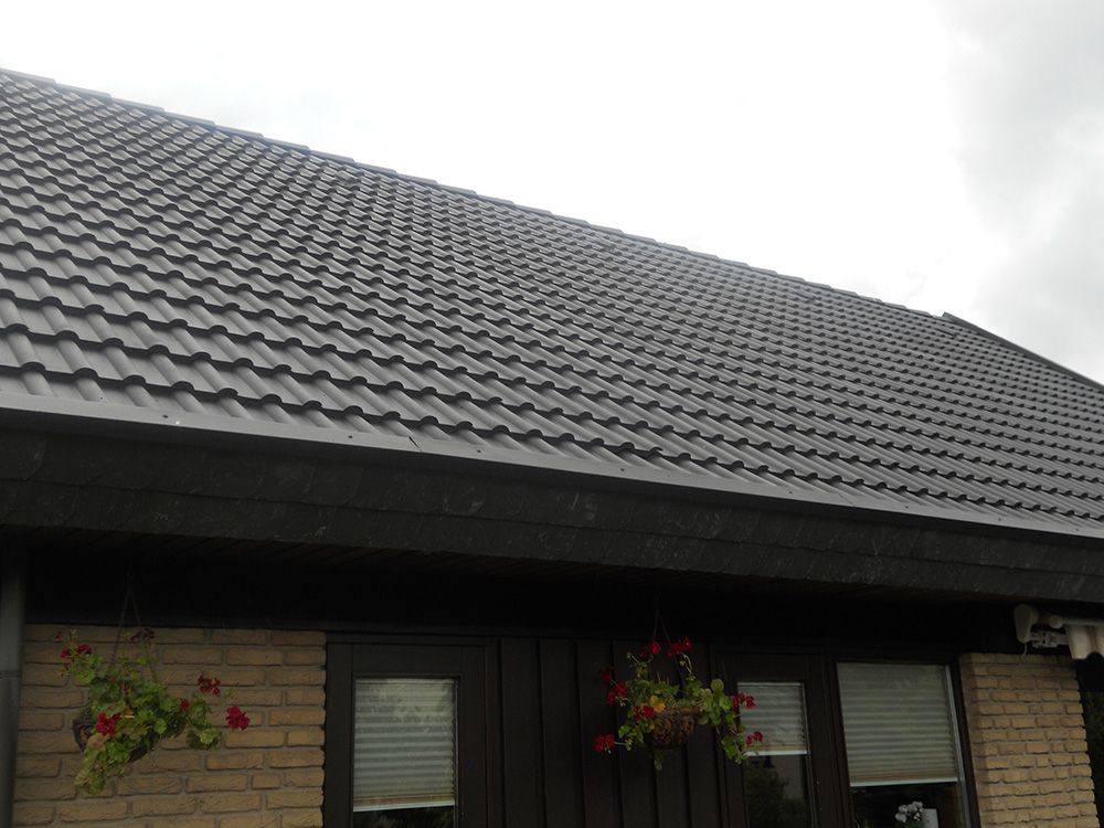 Ein Haus mit einem schwarzen Dach und Blumen davor.