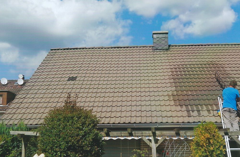 Ein Mann steht auf einer Leiter und reinigt das Dach eines Hauses.