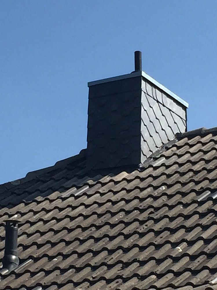 Ein Schornstein auf einem Ziegeldach mit einem blauen Himmel im Hintergrund.