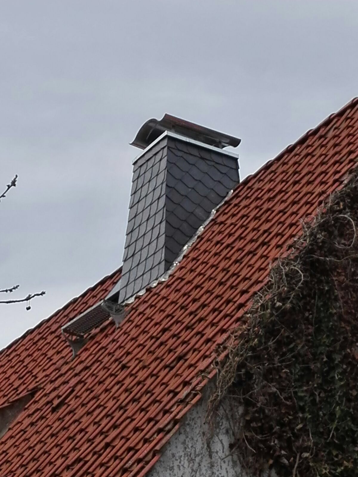 Auf einem roten Ziegeldach sitzt ein Schornstein.