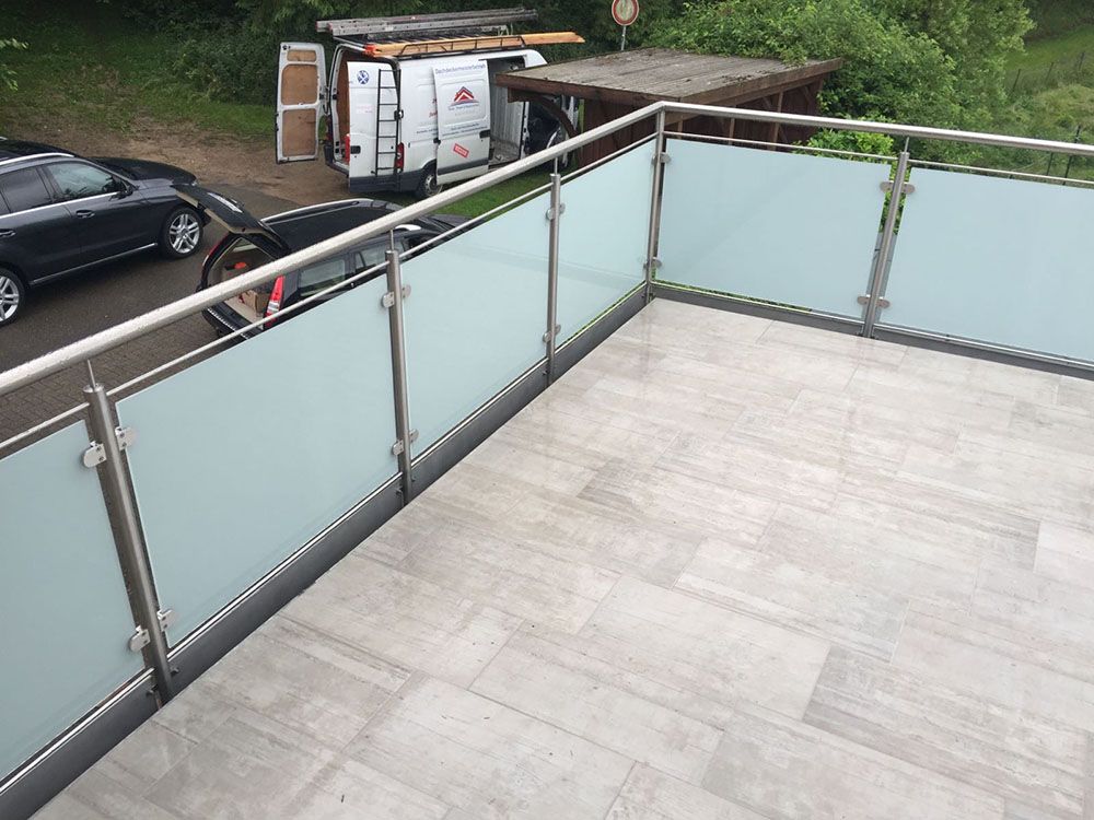 Ein Balkon mit einem Geländer aus Edelstahl und einem im Hintergrund geparkten Auto.