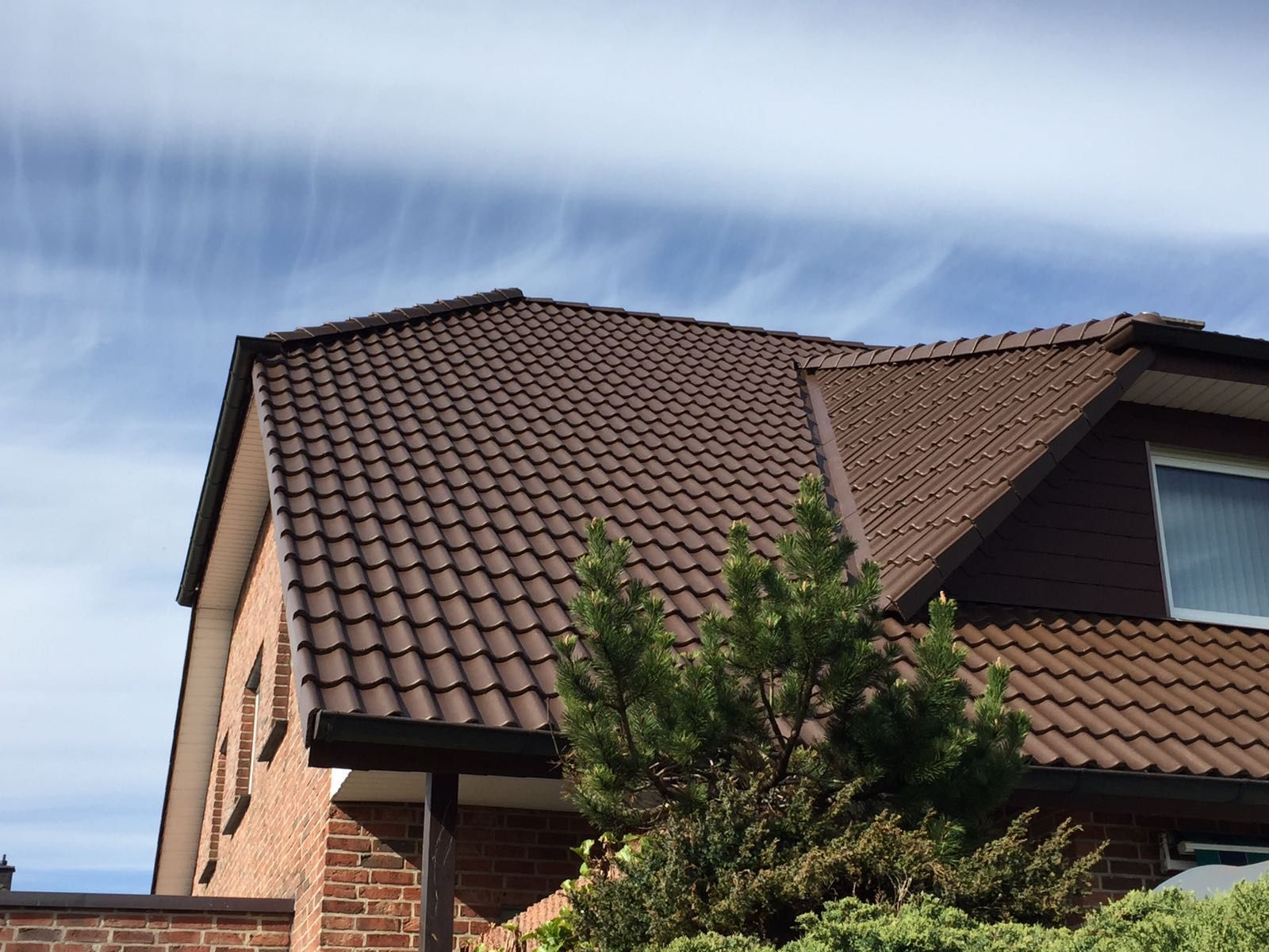 Ein Backsteinhaus mit einem braunen Dach und einem Baum davor