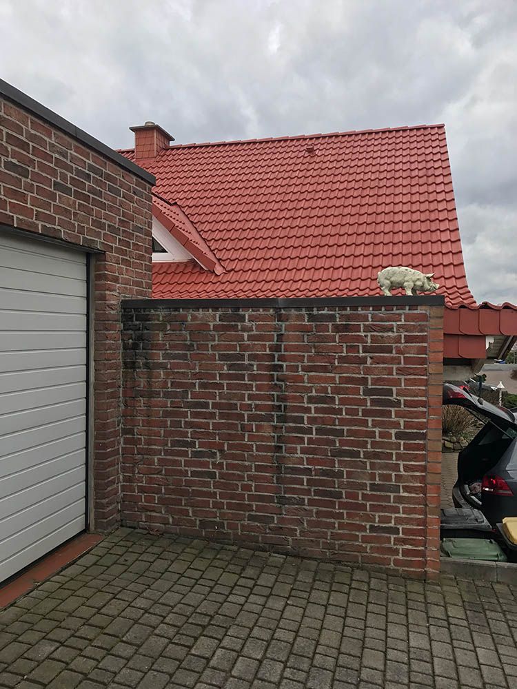 Eine Backsteinmauer neben einer Garage mit rotem Dach.