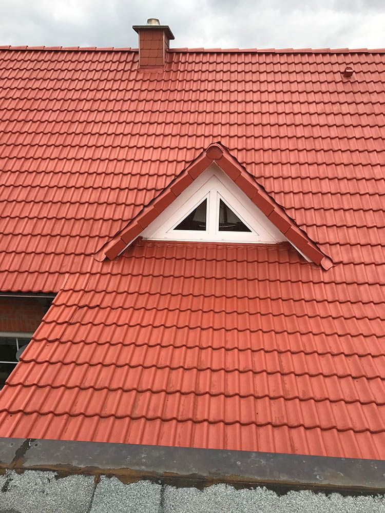 Ein rotes Ziegeldach mit einem weißen Dreiecksfenster