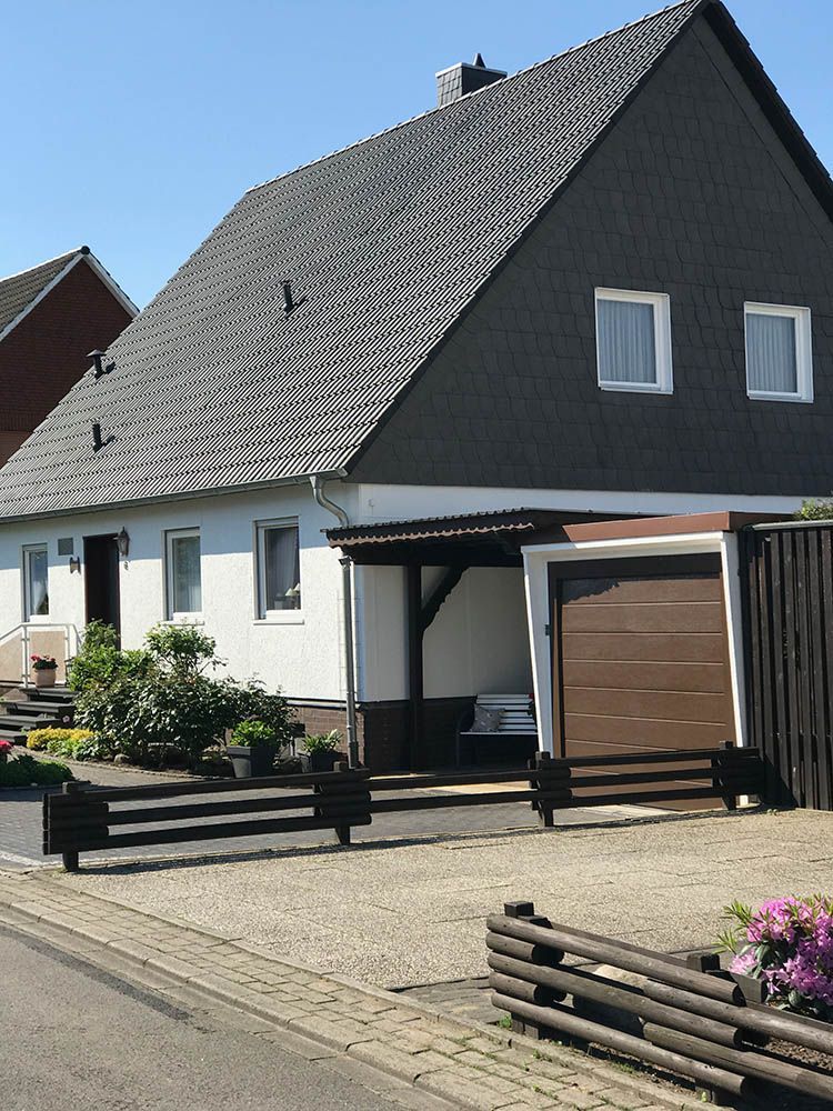 Ein weißes Haus mit schwarzem Dach und braunem Garagentor