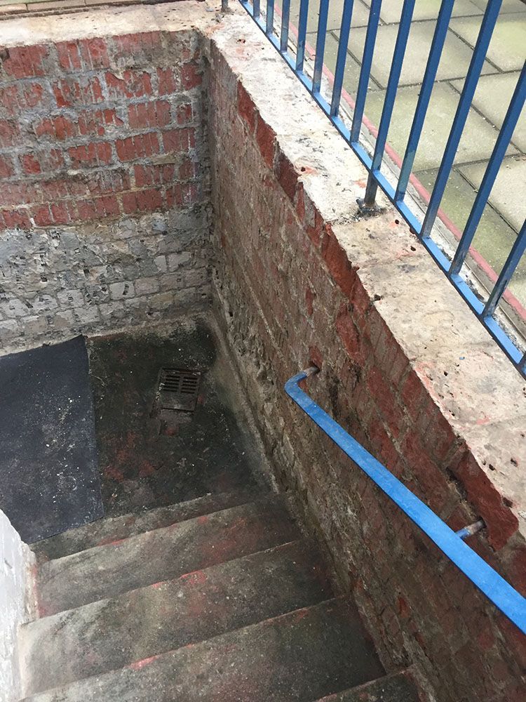 Eine Treppe führt zu einer Backsteinmauer mit einem blauen Geländer.