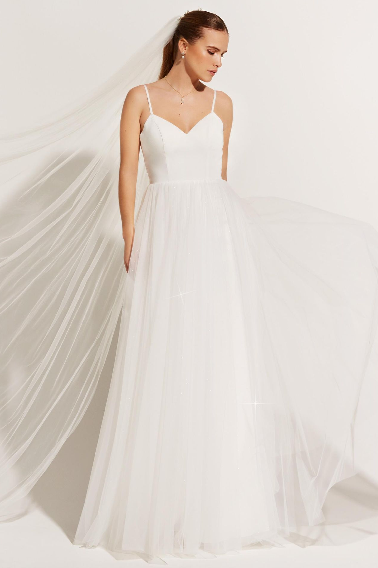 Eine Frau in einem weißen Brautkleid steht vor lila Blumen.