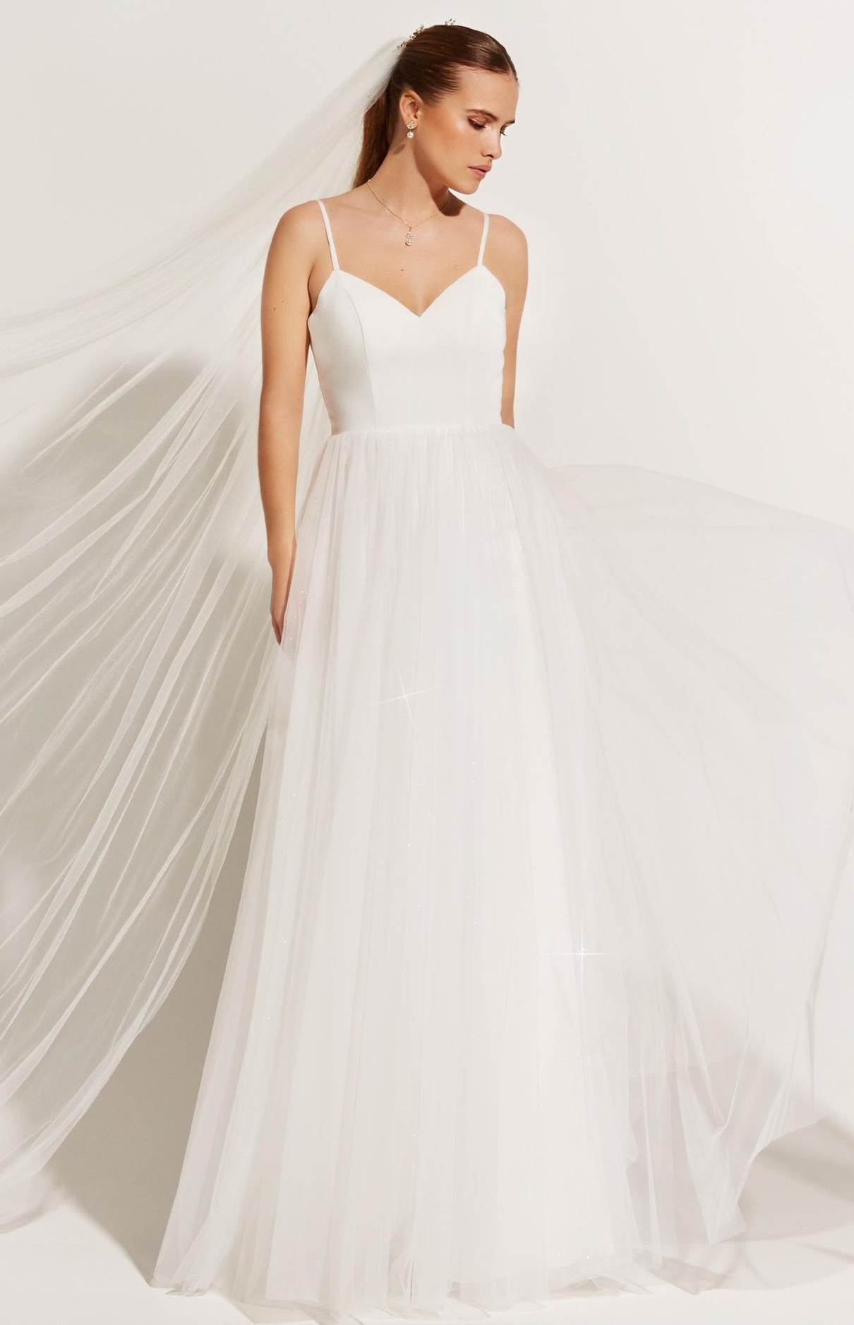 Eine Frau in einem weißen Brautkleid steht vor lila Blumen.