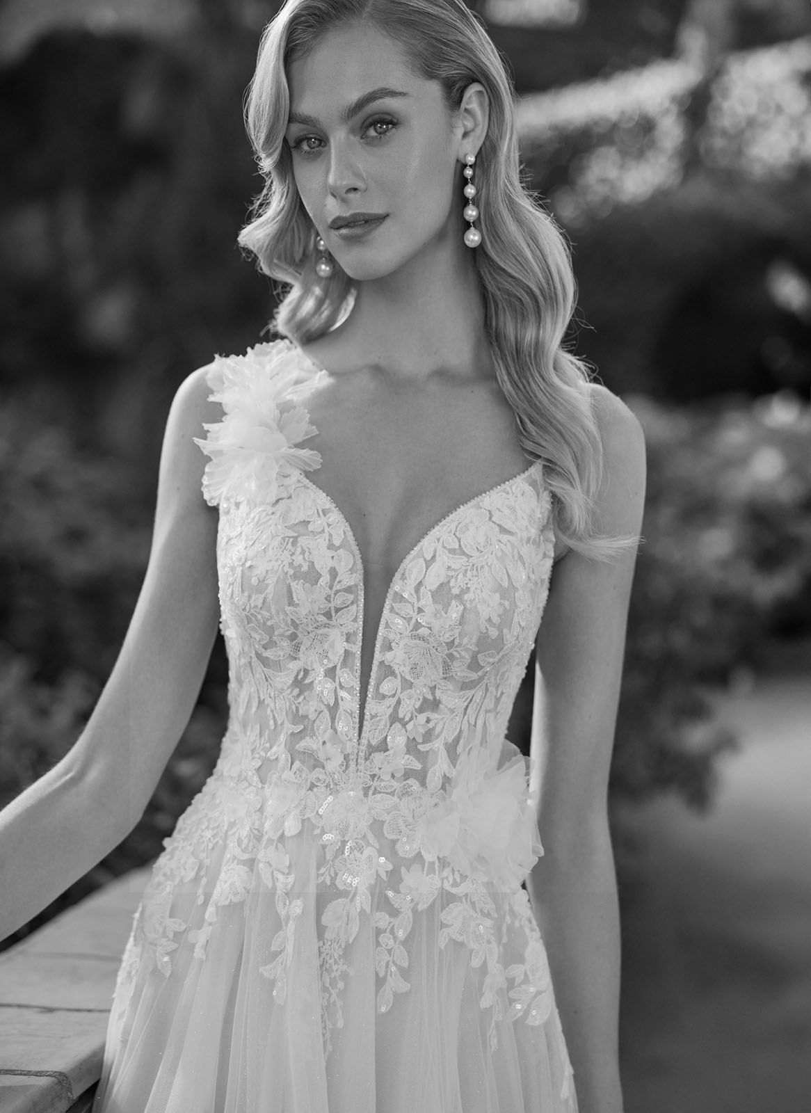 Eine Frau in einem weißen Kleid steht vor Blumen.
