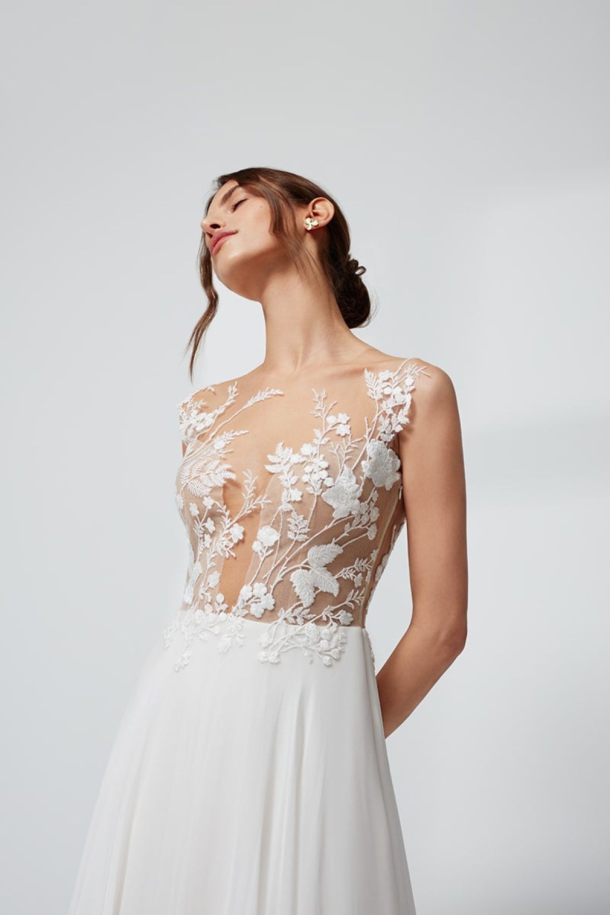 Eine Frau trägt ein weißes Brautkleid mit einem Oberteil aus geblümter Spitze.