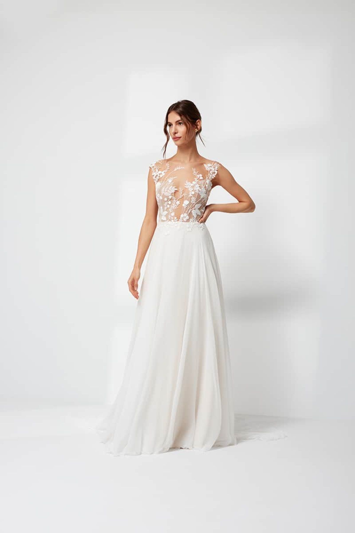 Eine Frau in einem weißen Brautkleid steht vor einer weißen Wand.