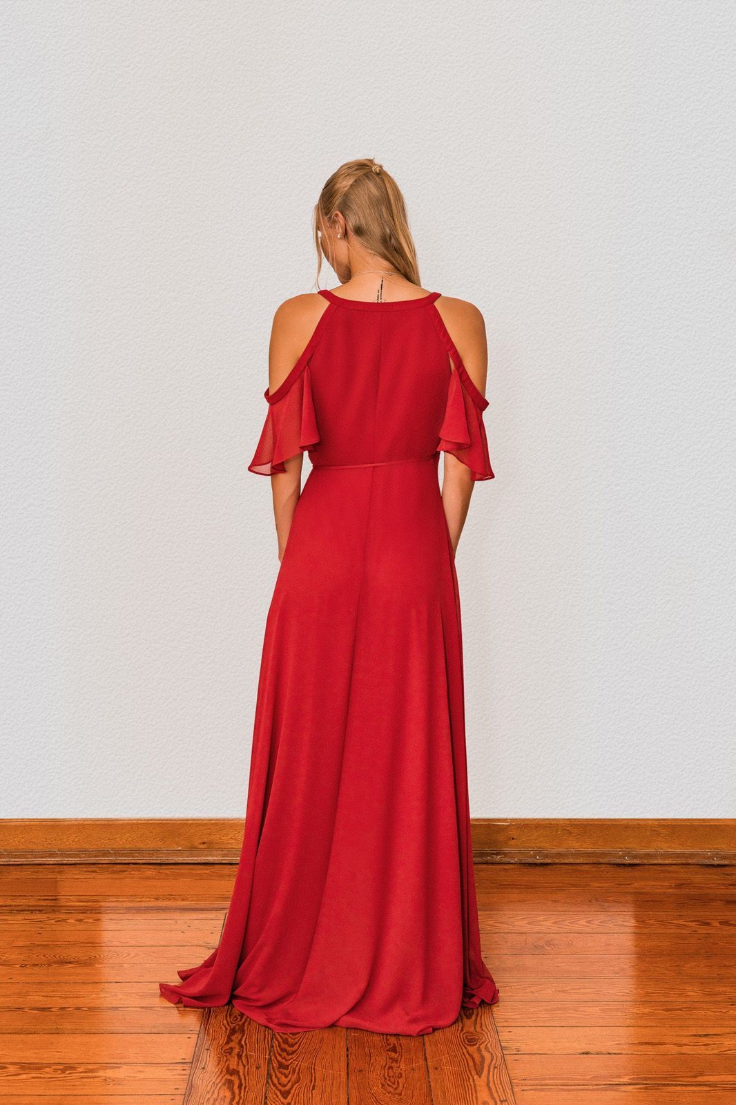 Der Rücken einer Frau in einem roten Kleid steht auf einem Holzboden.