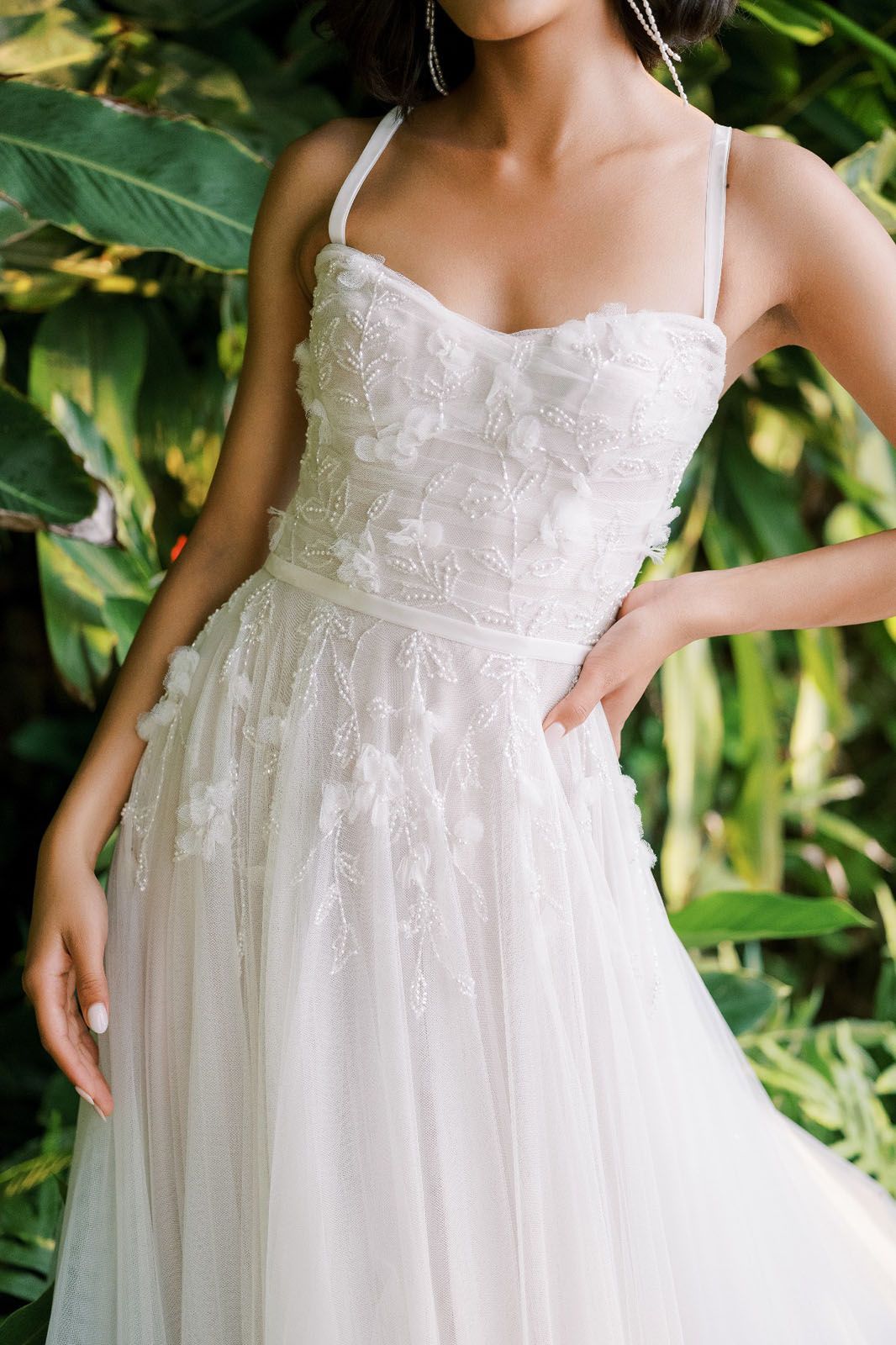 Eine Frau in einem weißen Kleid steht vor Blumen.