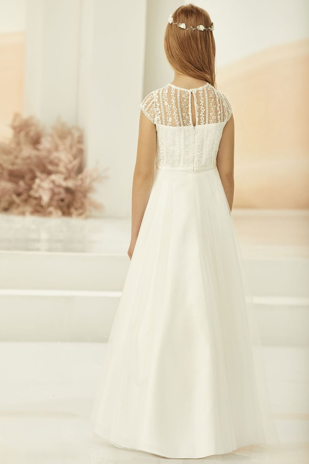 Ein kleines Mädchen trägt ein weißes Erstkommunionkleid.