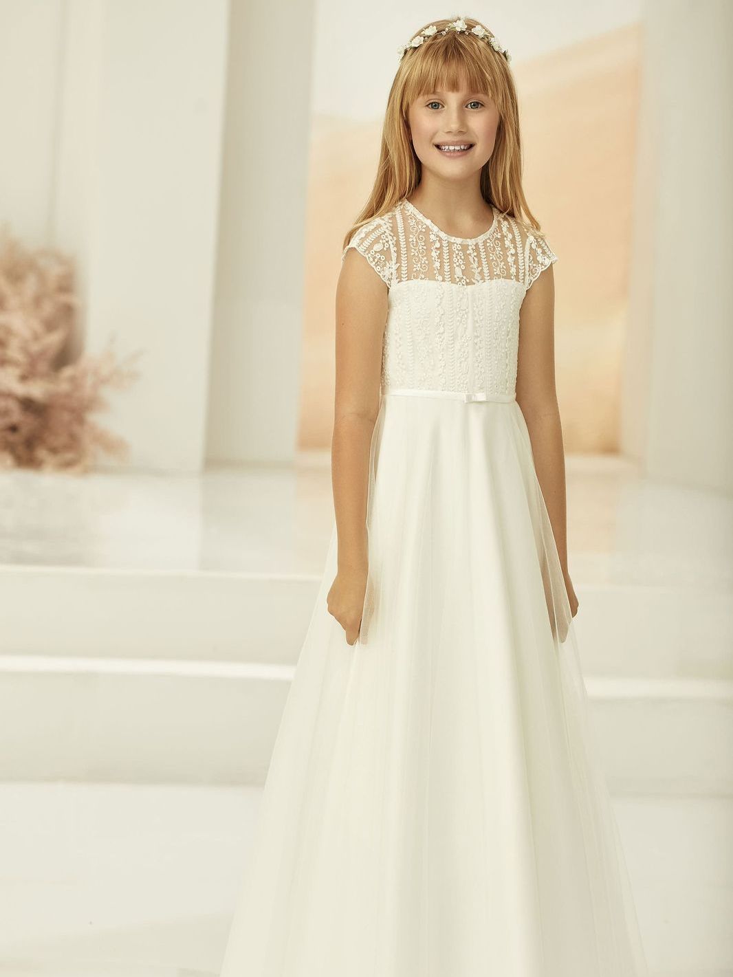 Ein kleines Mädchen trägt ein weißes Erstkommunionkleid.