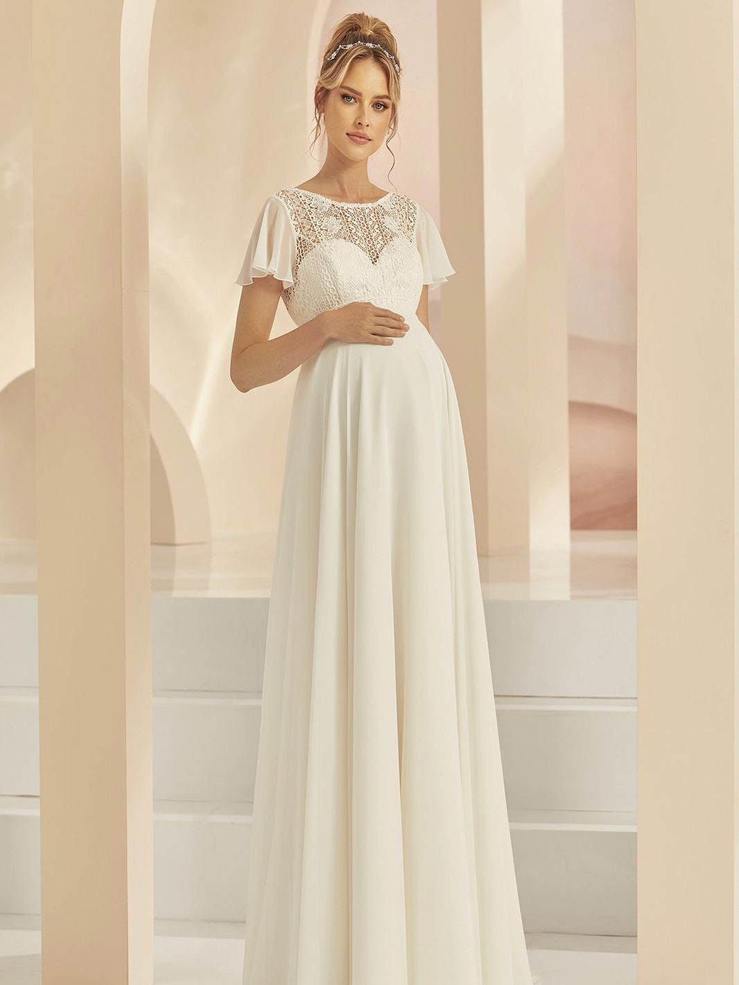Eine schwangere Frau trägt ein weißes Brautkleid.