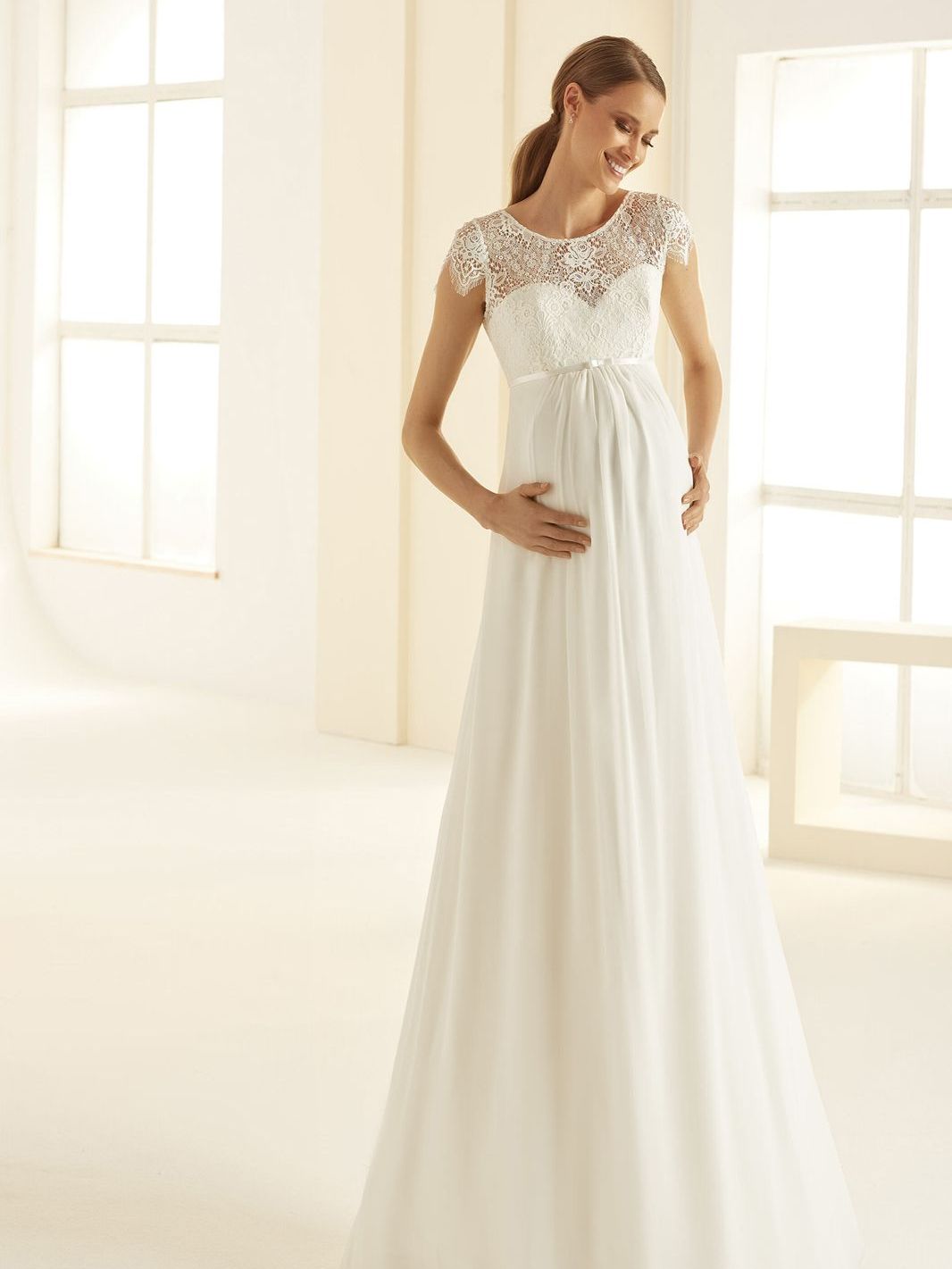 Eine schwangere Frau trägt ein weißes Brautkleid.