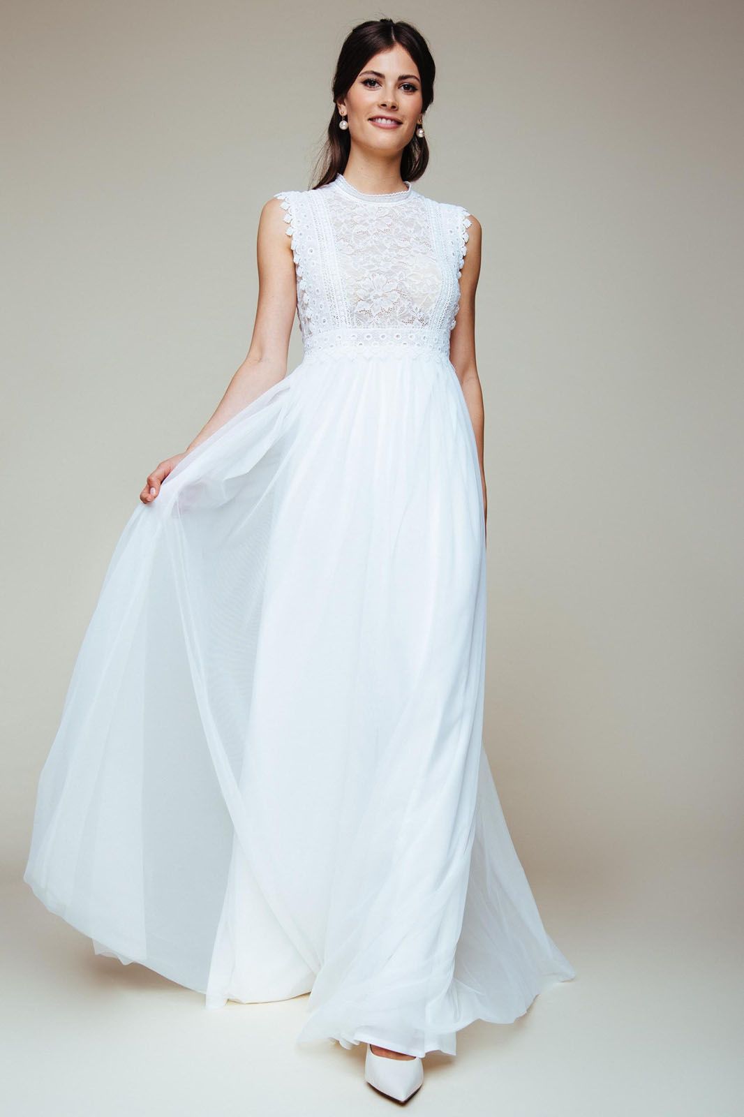 Eine Frau in einem weißen Brautkleid steht vor lila Blumen.