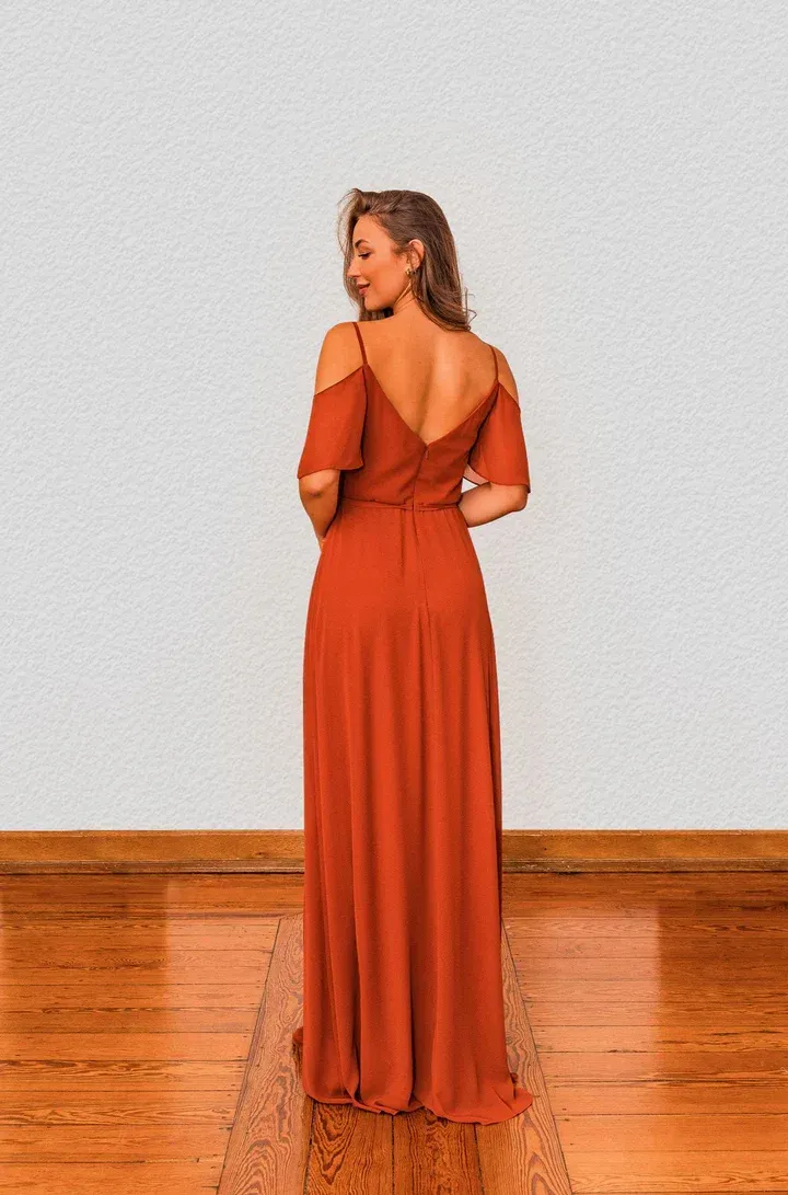 Eine Frau in einem langen orangefarbenen Kleid steht auf einem Holzboden.