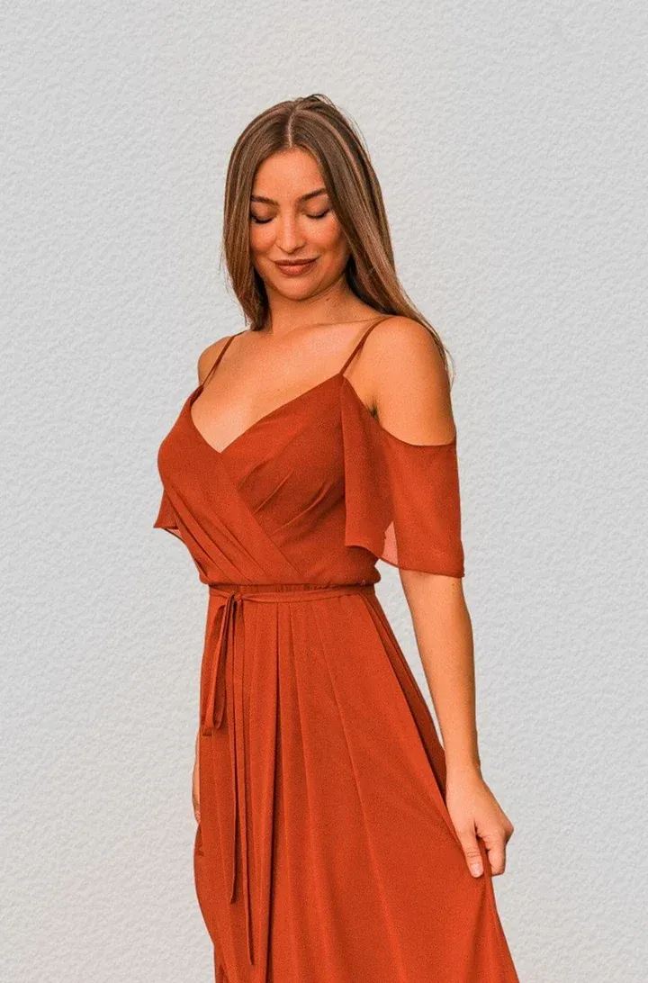Eine Frau in einem orangefarbenen Kleid steht vor einem weißen Hintergrund.