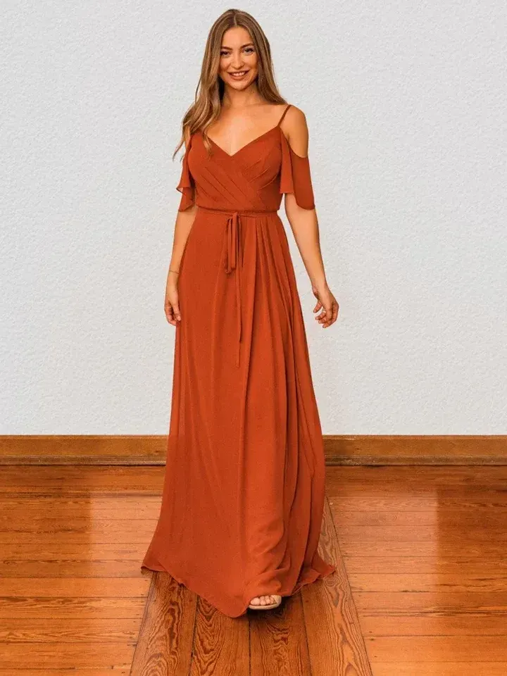 Eine Frau in einem langen orangefarbenen Kleid steht auf einem Holzboden.