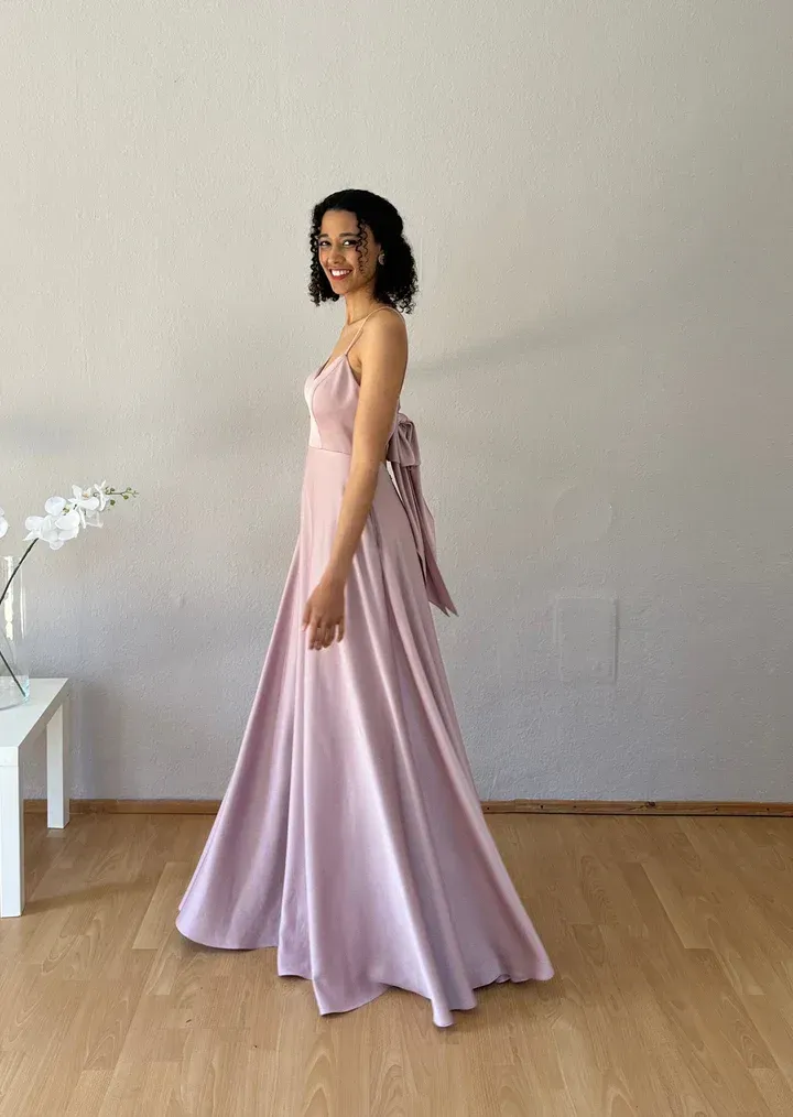 Eine Frau in einem langen rosa Kleid steht auf einem Holzboden.