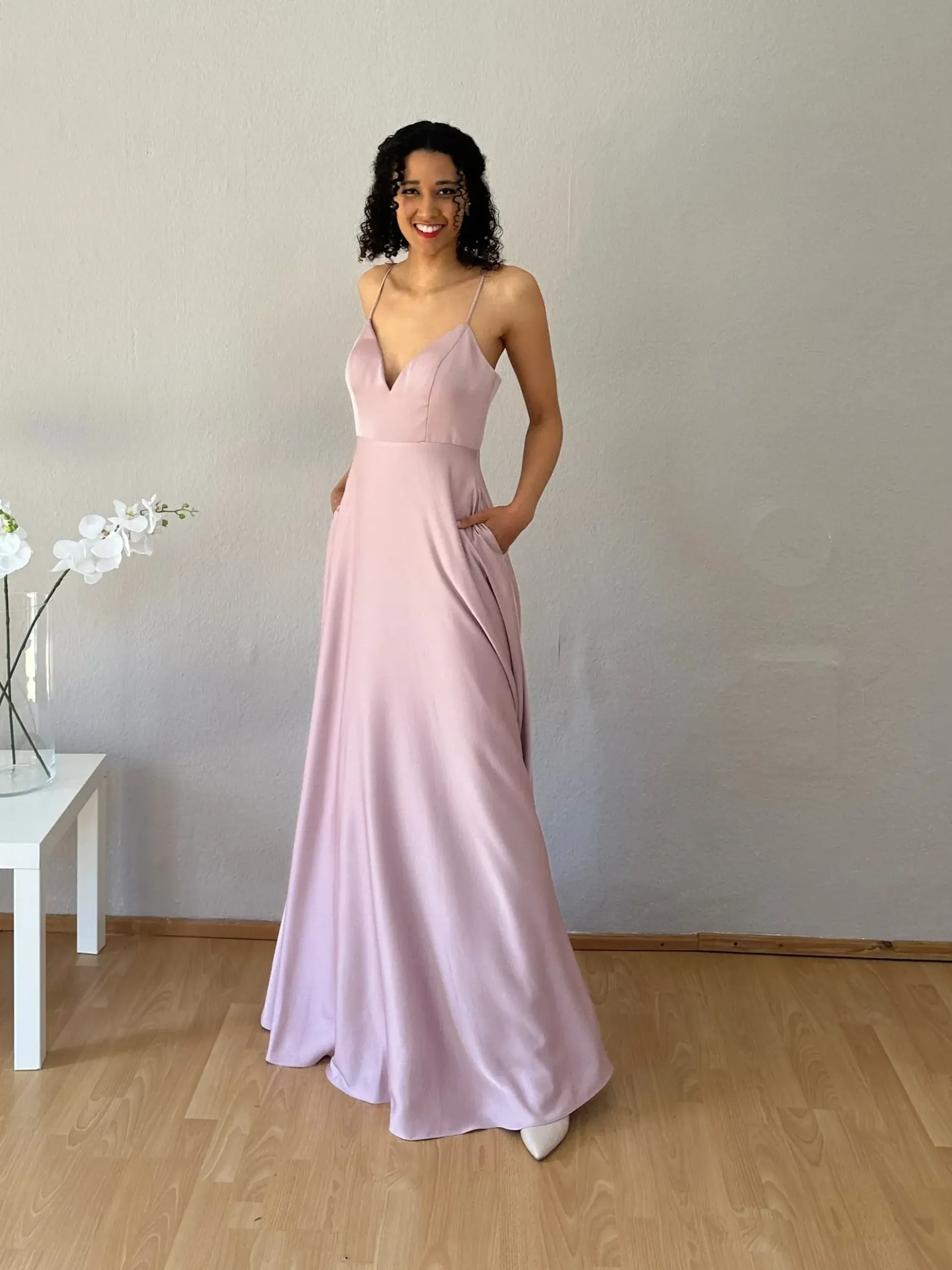 Eine Frau in einem langen rosa Kleid steht auf einem Holzboden.