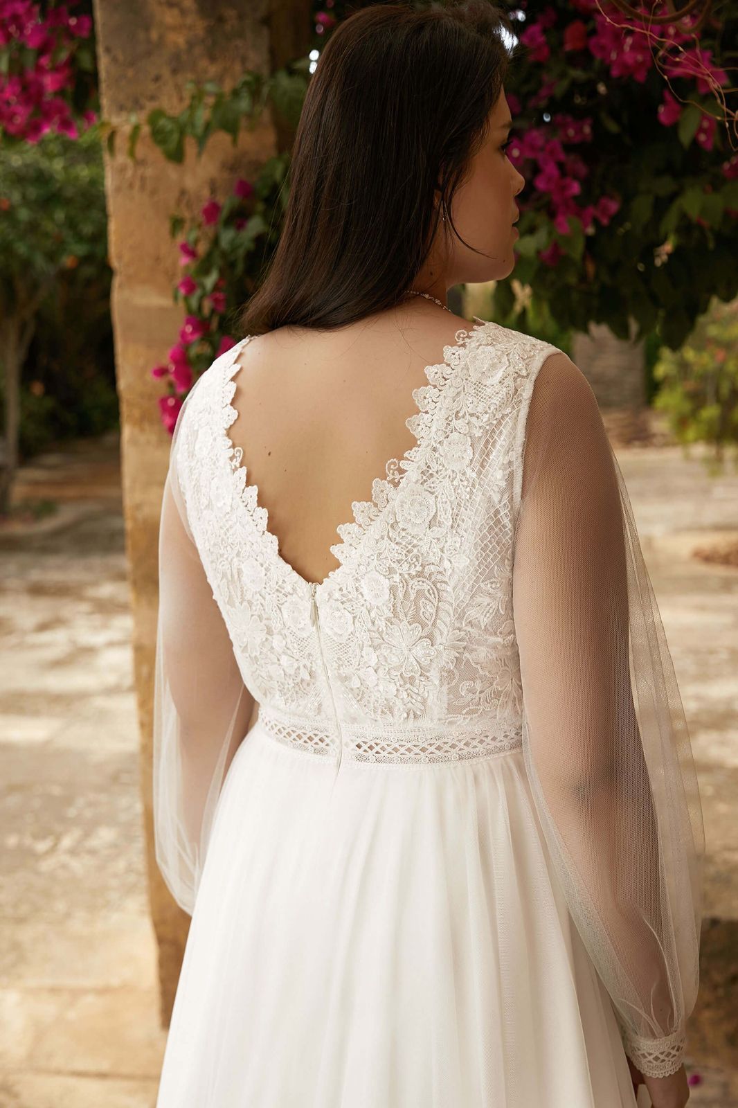 Eine Frau in einem Brautkleid steht mit einem Glas Wein neben einem Tisch.