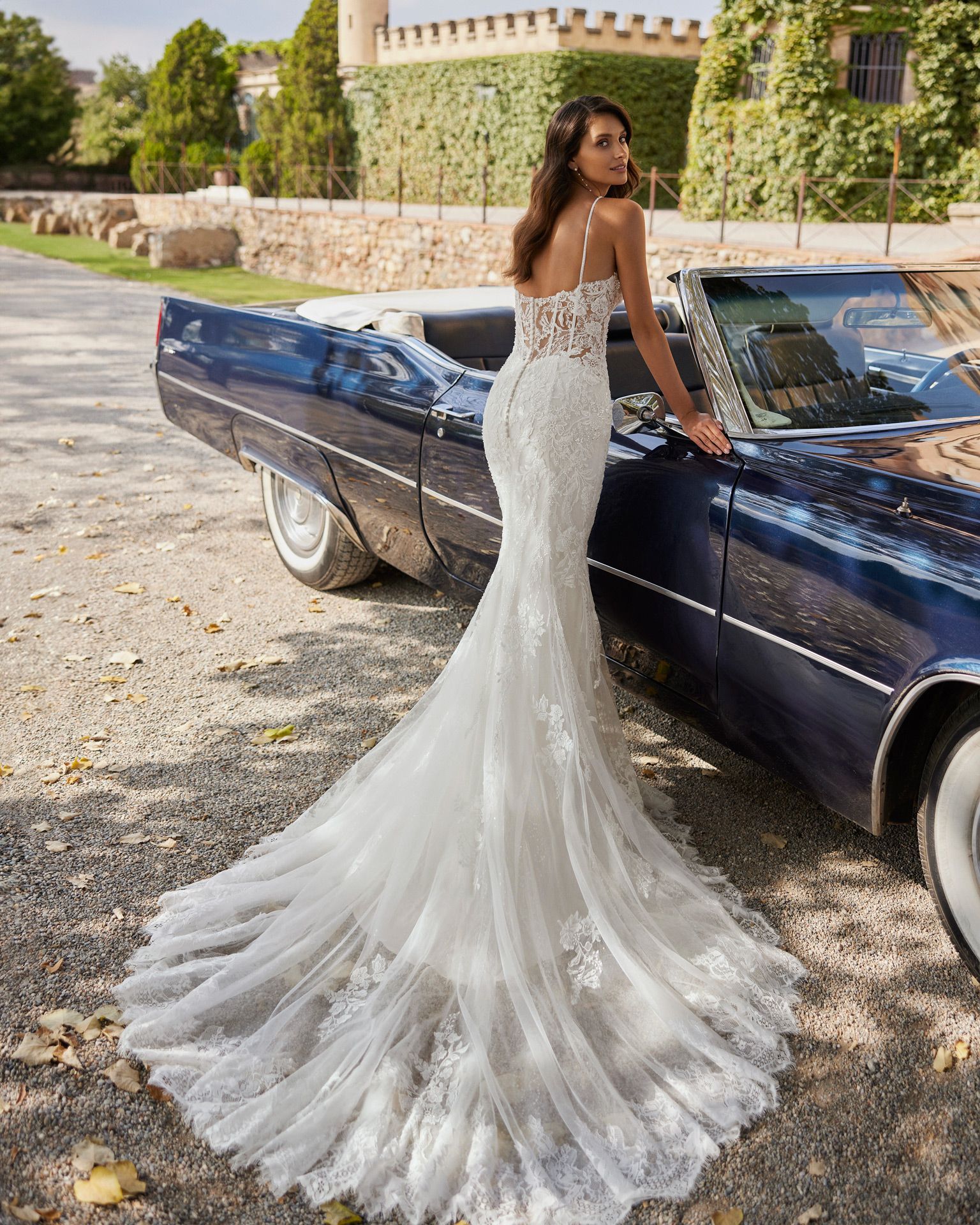 Eine Frau in einem Brautkleid steht neben einem blauen Auto.
