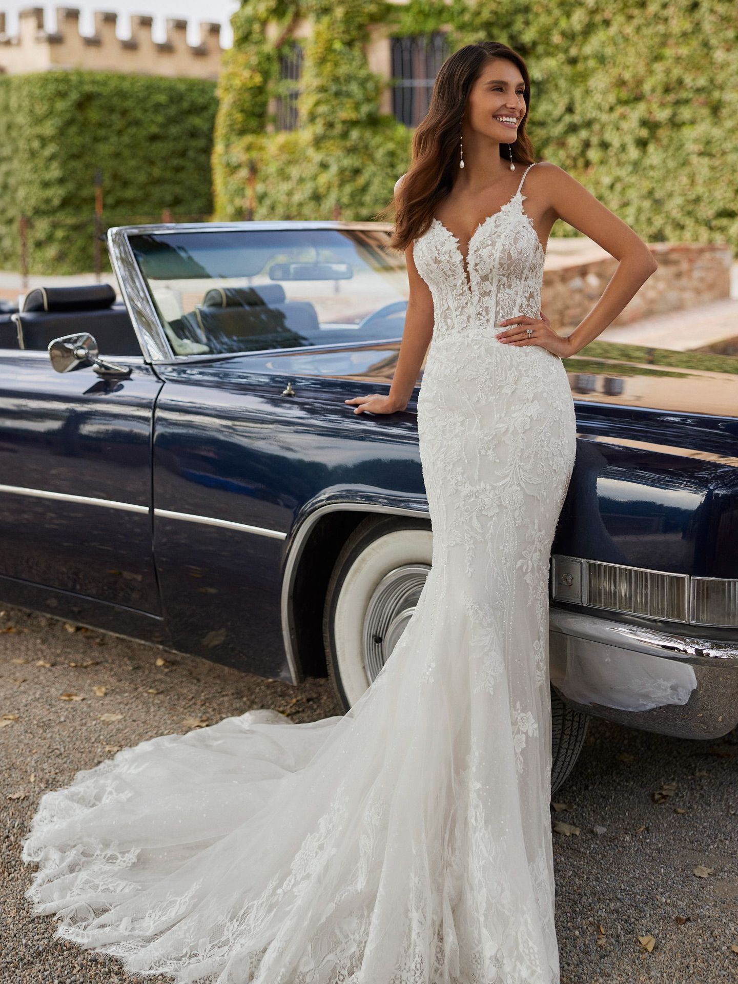 Eine Frau in einem Brautkleid lehnt an einem blauen Auto.