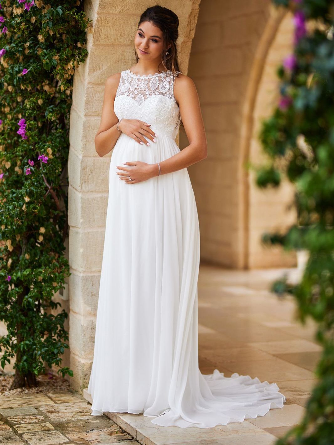 Eine schwangere Frau trägt ein weißes Brautkleid und hält ihren Bauch.