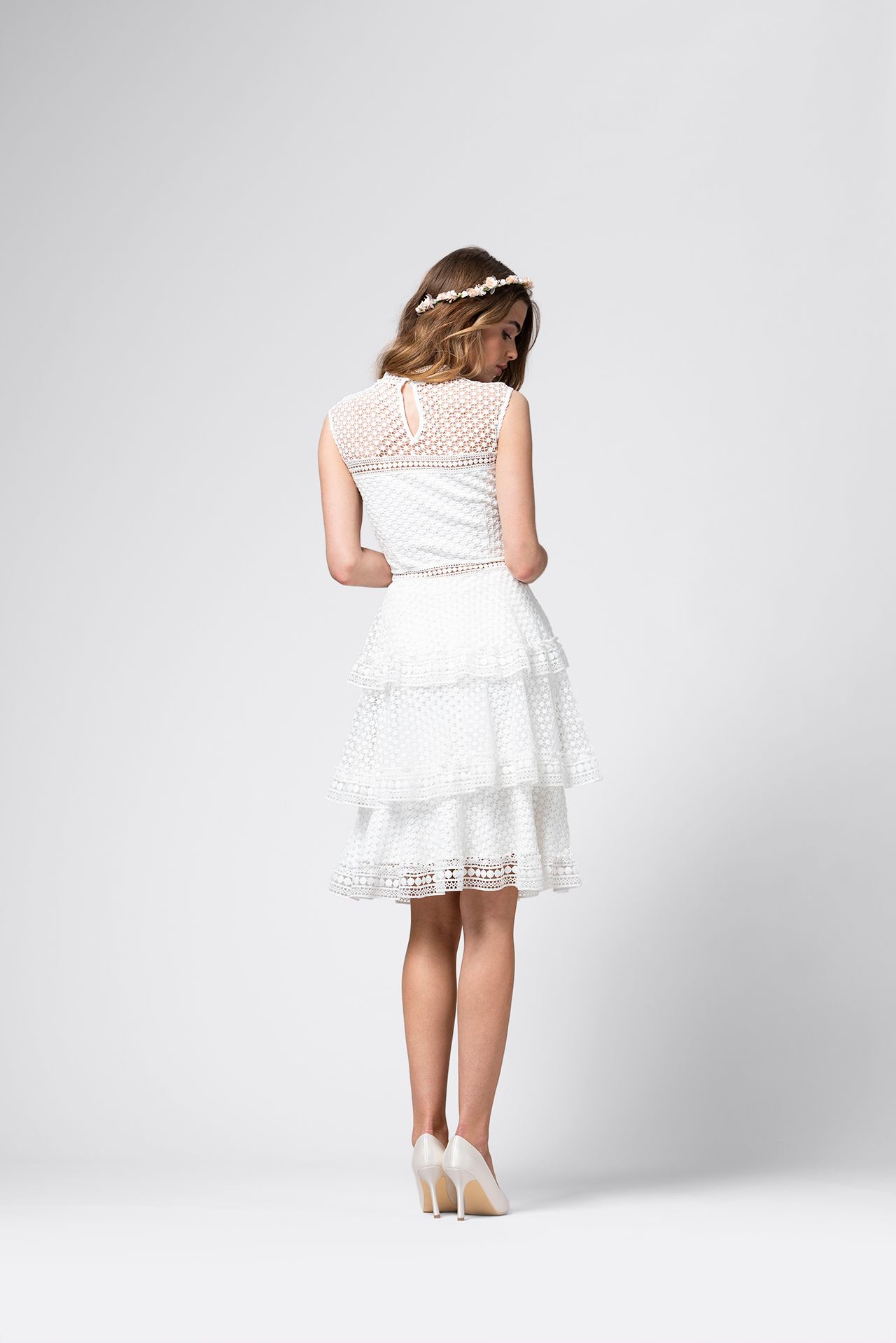 Der Rücken einer Frau, die ein weißes Spitzenkleid und High Heels trägt.