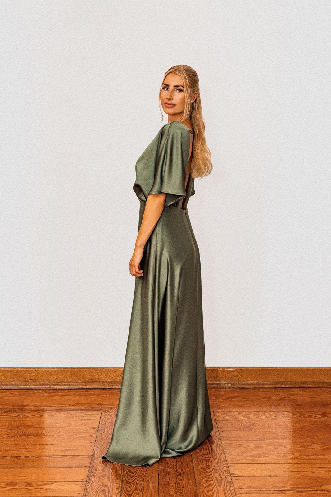 Eine Frau in einem langen grünen Kleid steht auf einem Holzboden.