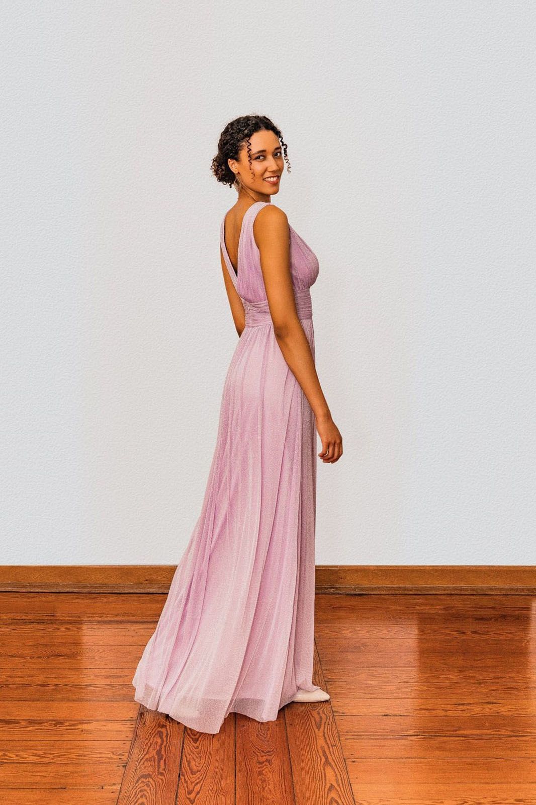 Eine Frau in einem langen rosa Kleid steht auf einem Holzboden.