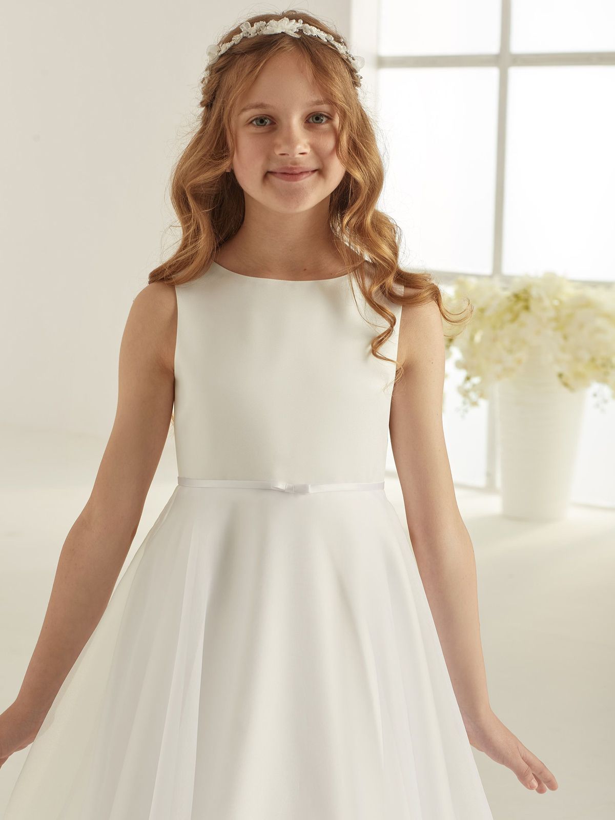 Ein kleines Mädchen trägt ein weißes Kleid und einen Blumenkranz.