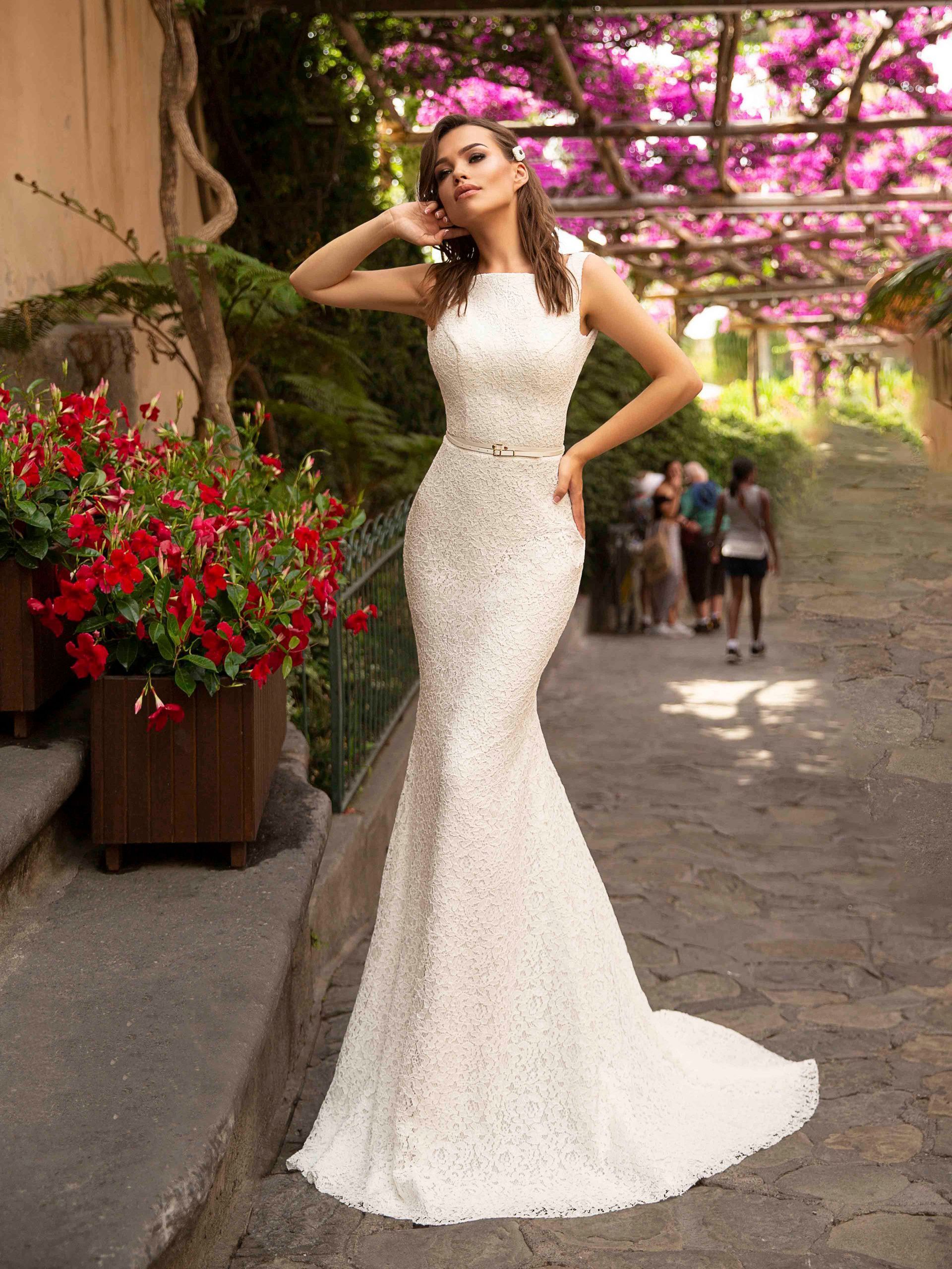 Eine Frau in einem weißen Brautkleid steht vor lila Blumen.