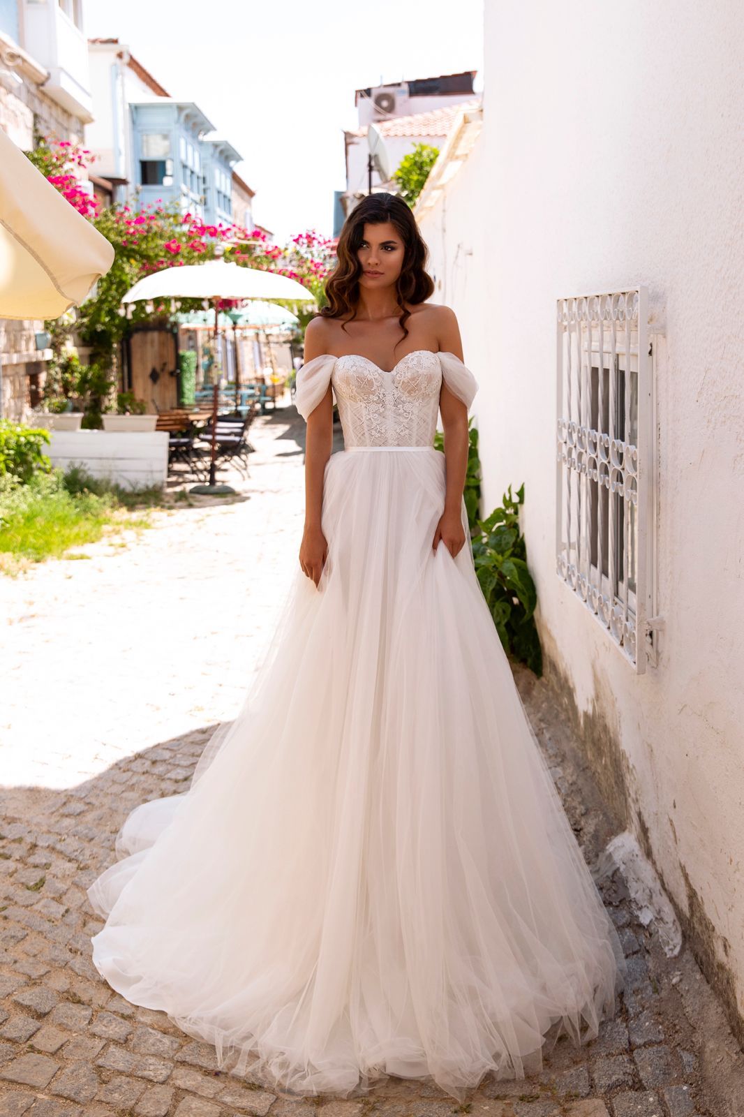 Eine Frau in einem weißen Brautkleid steht vor lila Blumen.