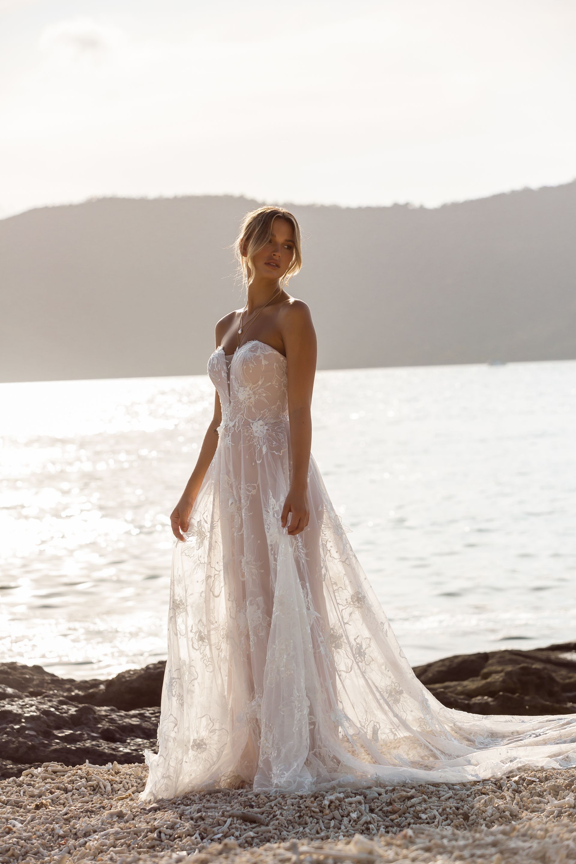 Eine Frau in einem Brautkleid steht neben einem Tisch und Stühlen am Strand.