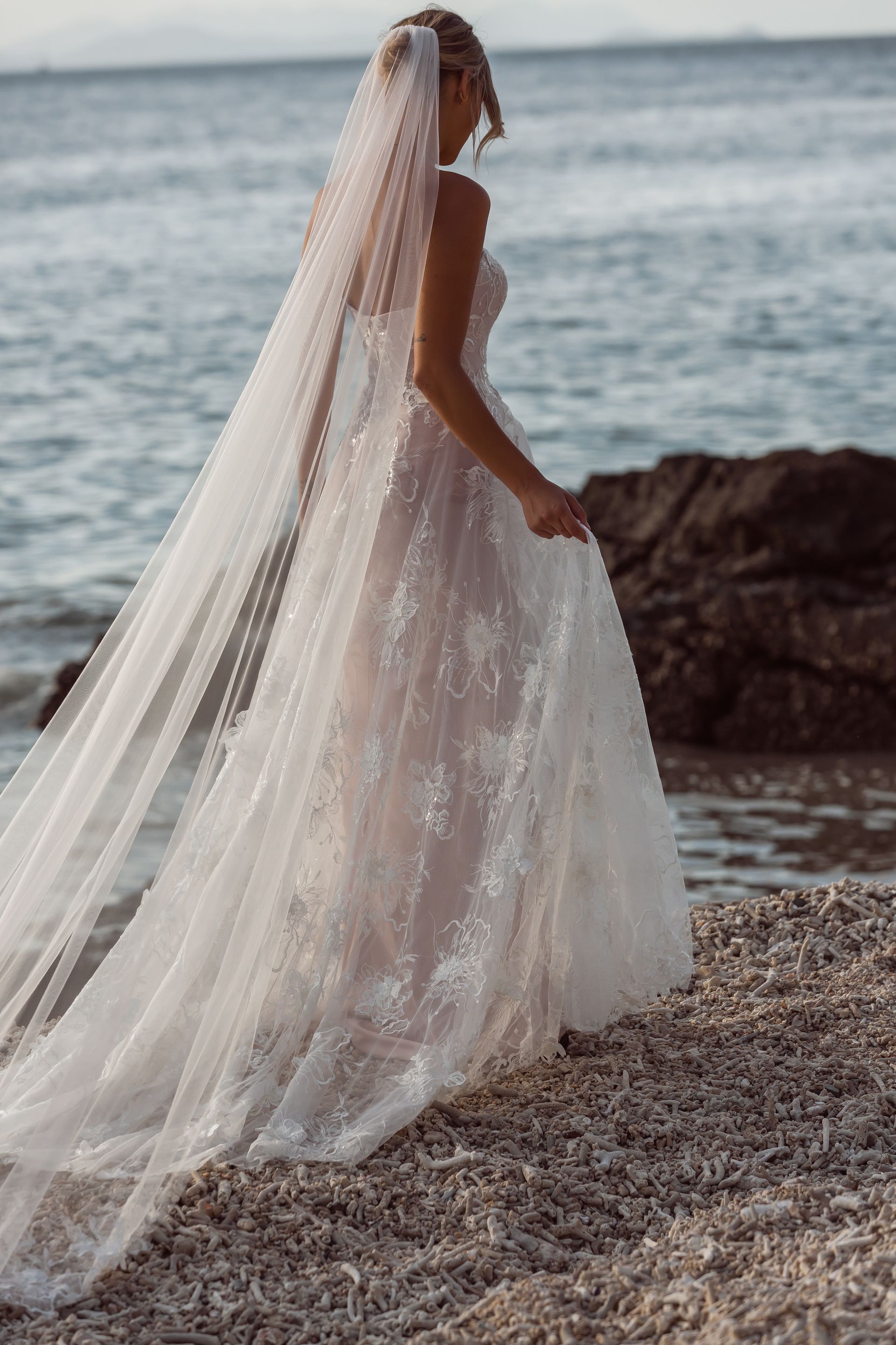 Eine Frau in einem Brautkleid steht neben einem Tisch und Stühlen am Strand.