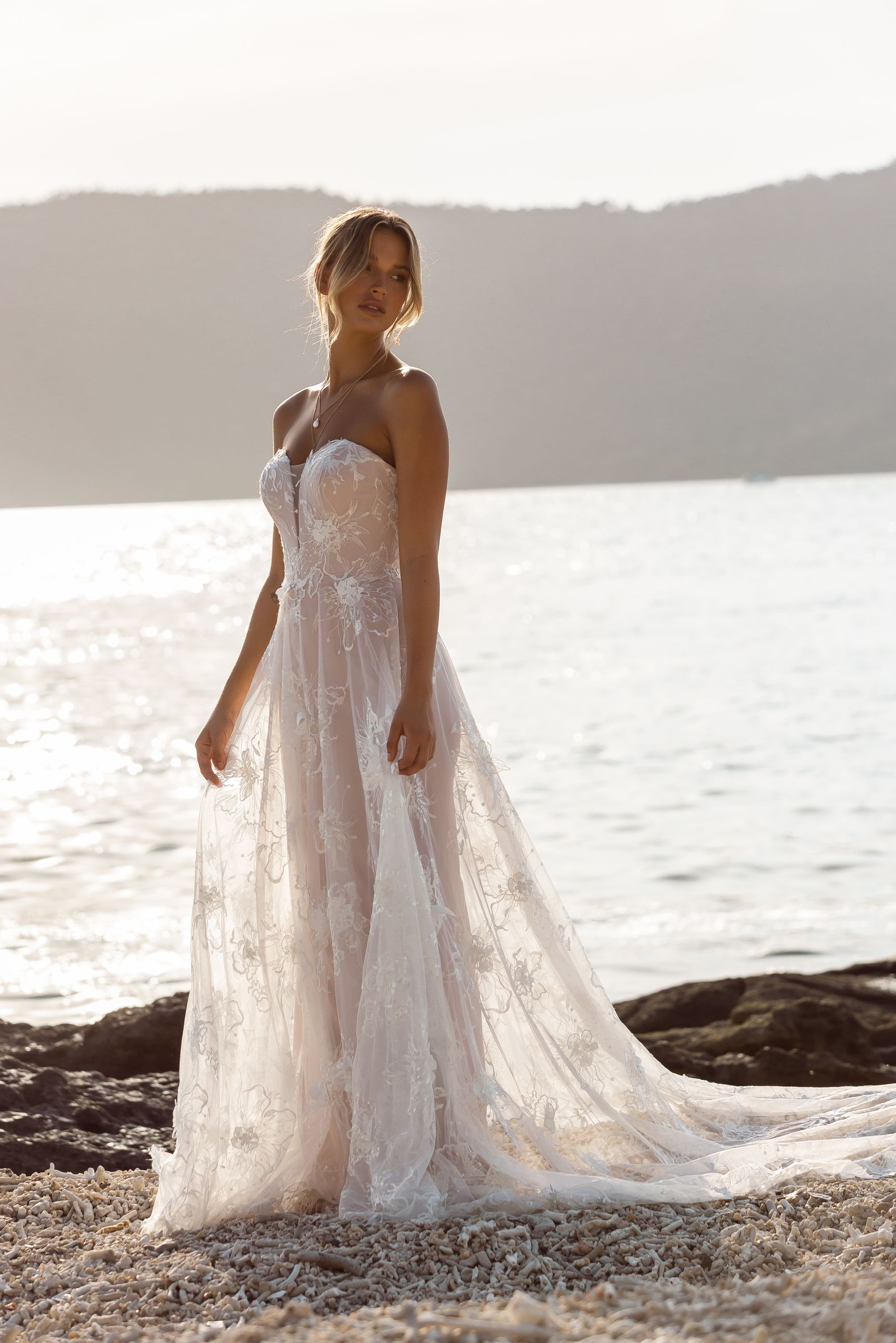 Eine Frau in einem Brautkleid steht neben einem Tisch und Stühlen am Strand.