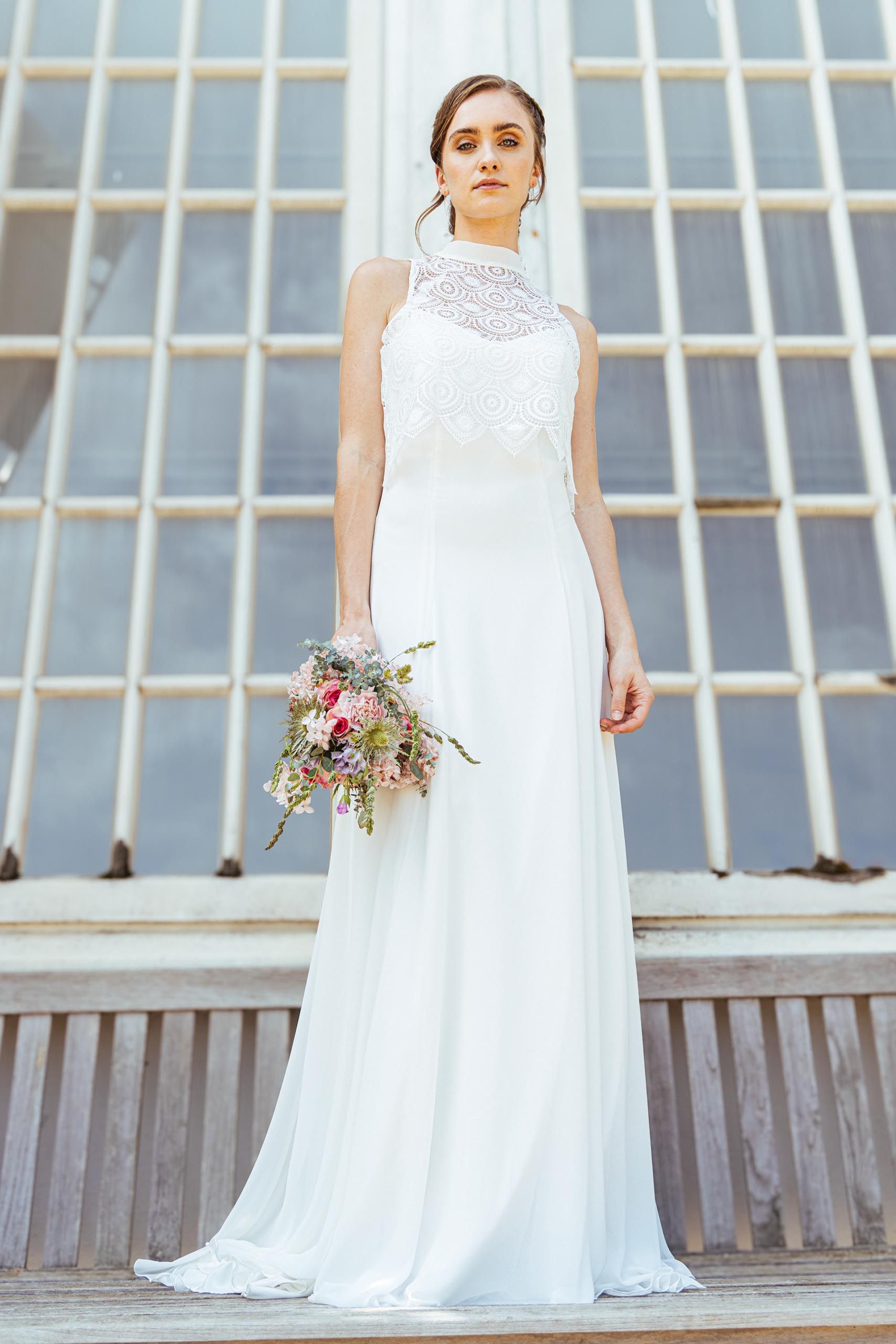 Eine Frau in einem weißen Brautkleid steht vor lila Blumen.