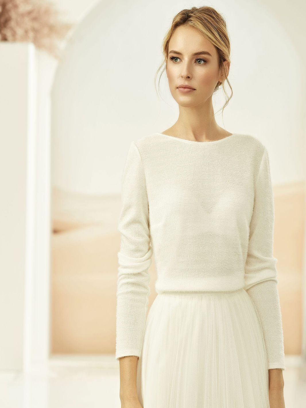 Eine Frau in einem weißen Kleid mit langen Ärmeln steht in einem Raum.