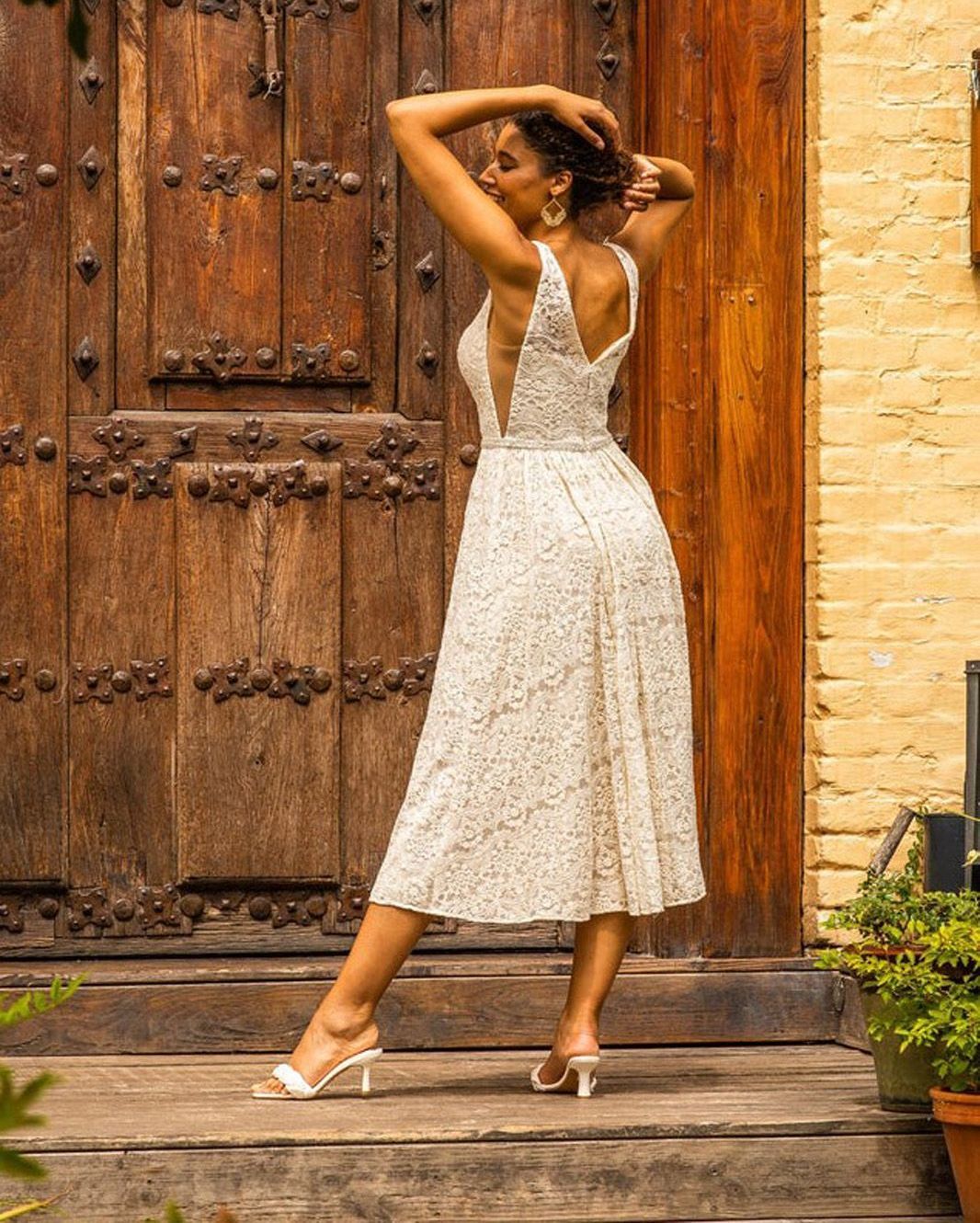 Eine Frau in einem weißen Kleid steht vor einer Holztür.