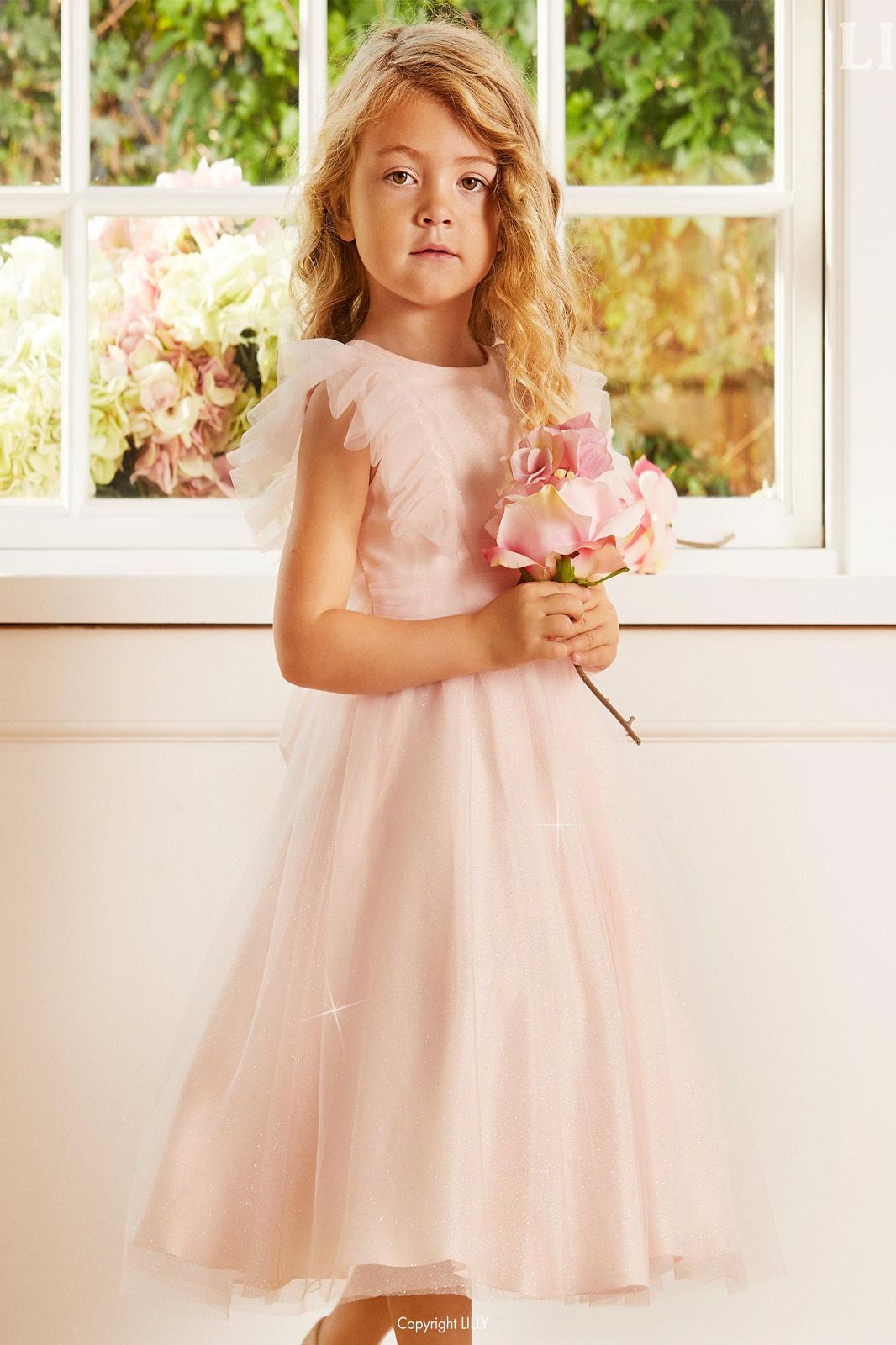 Ein kleines Mädchen in einem rosa Kleid hält einen Blumenstrauß.