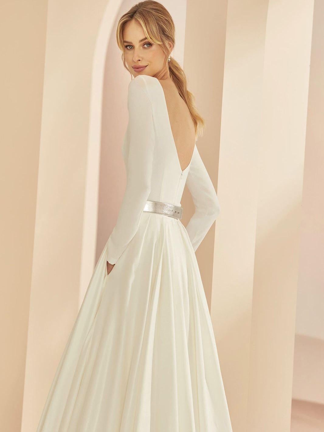 Eine Frau trägt ein weißes Brautkleid mit langen Ärmeln und V-Ausschnitt.
