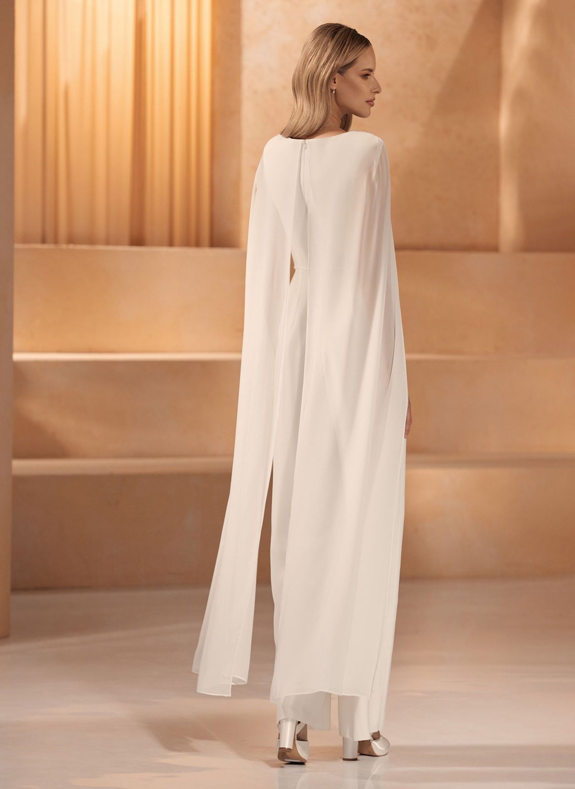 Eine Frau in einem weißen Brautkleid steht vor einer Steinmauer.