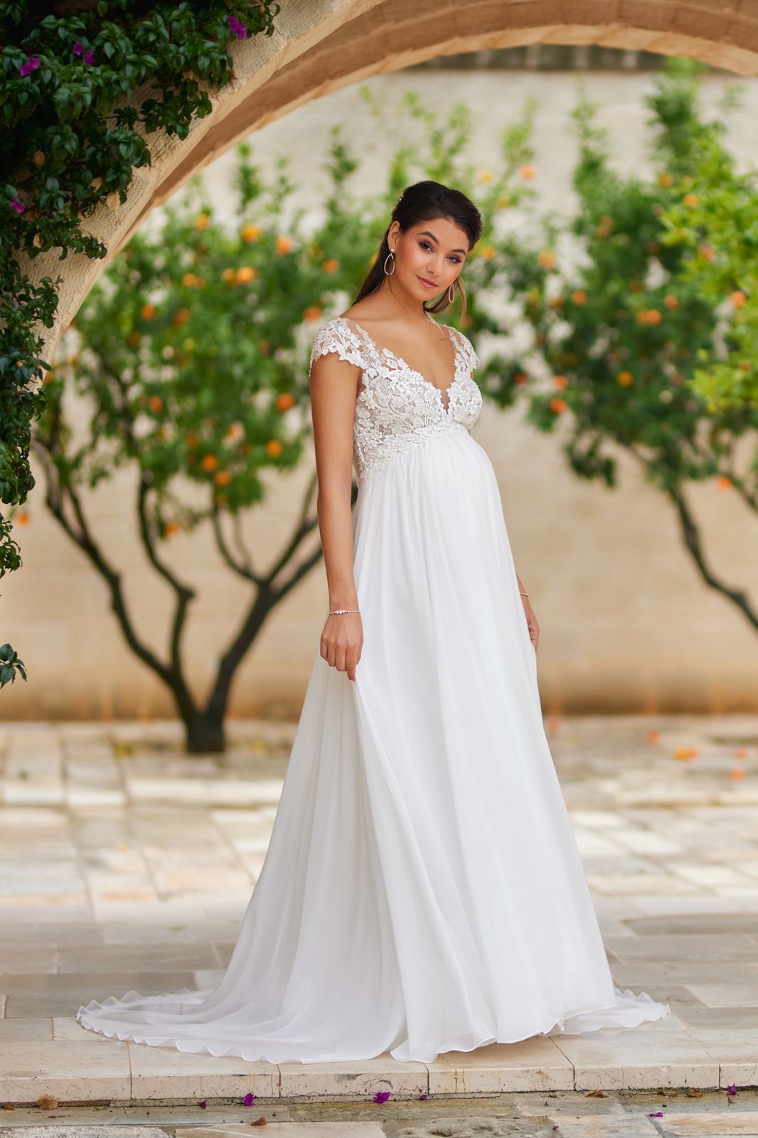 Eine schwangere Frau trägt ein weißes Brautkleid.