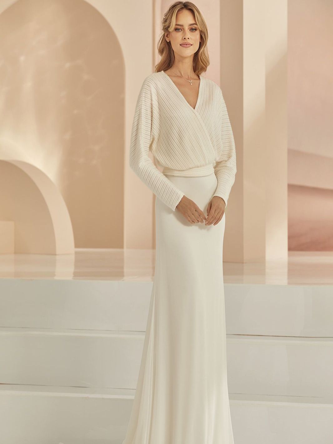 Eine Frau trägt ein weißes Brautkleid mit langen Ärmeln.