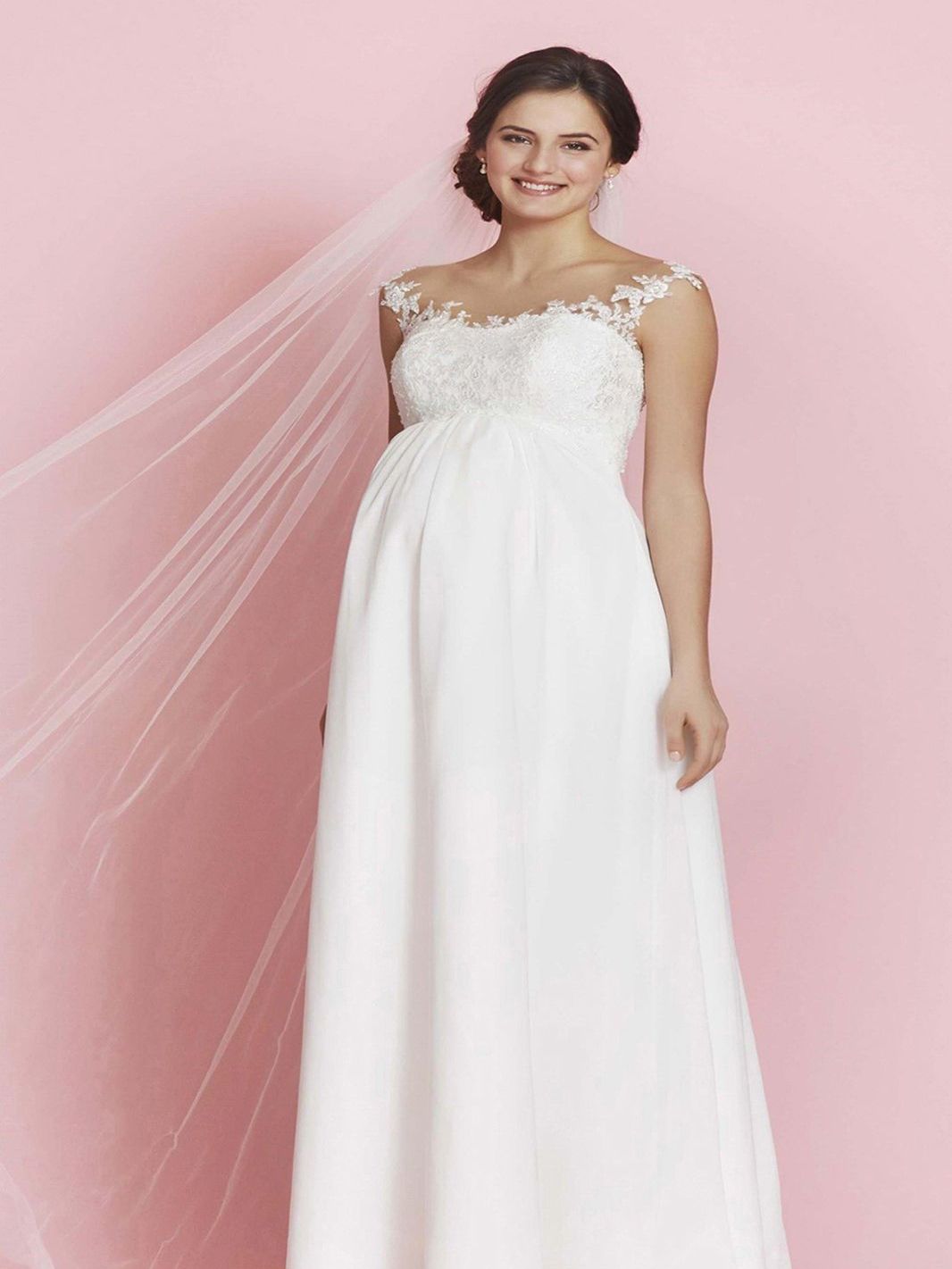 Eine schwangere Frau trägt ein weißes Brautkleid und einen Schleier.